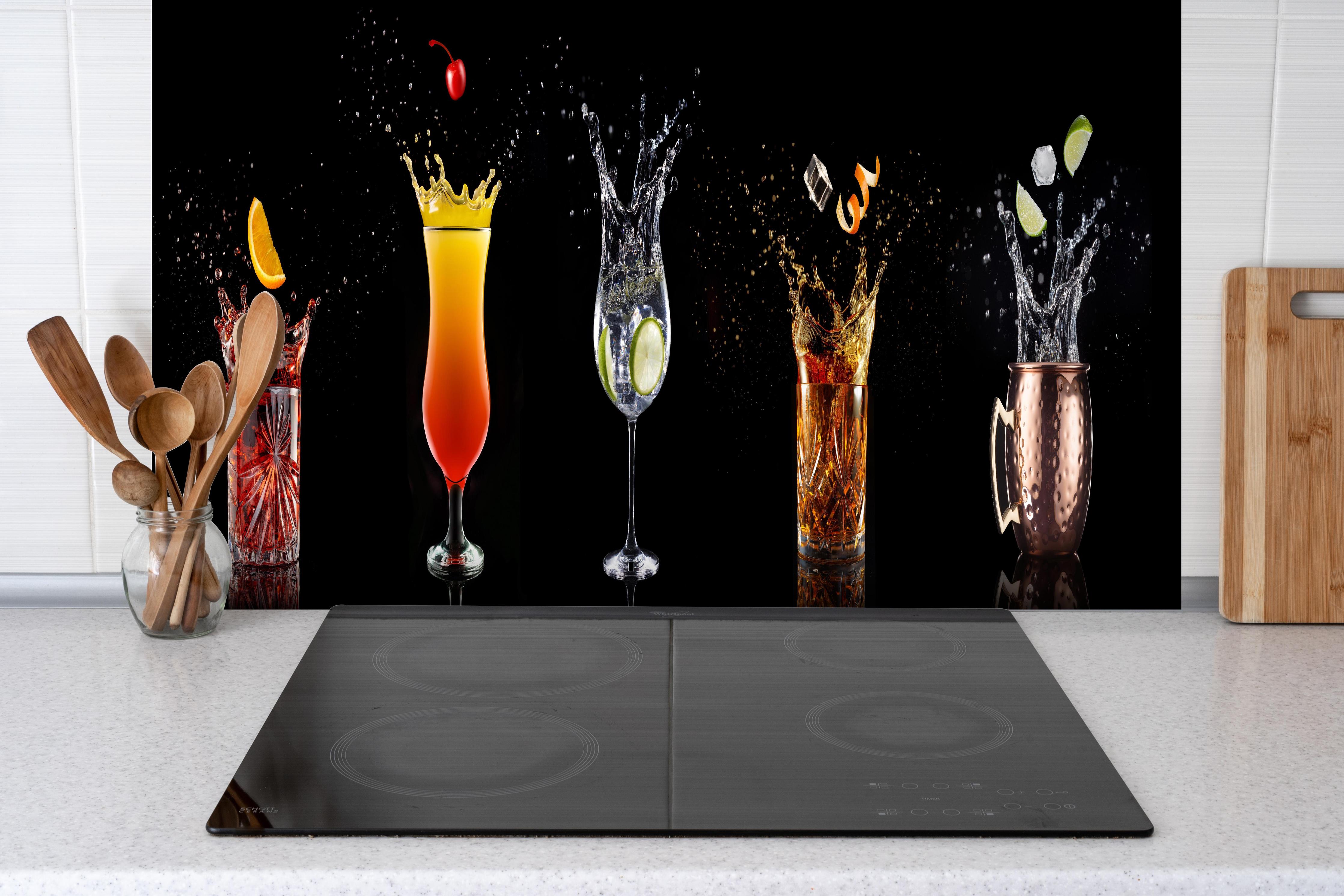 Spritzschutz - Splash-Effekt mit Cocktails auf Schwarz hinter einem Cerankochfeld zwischen Holz-Kochutensilien