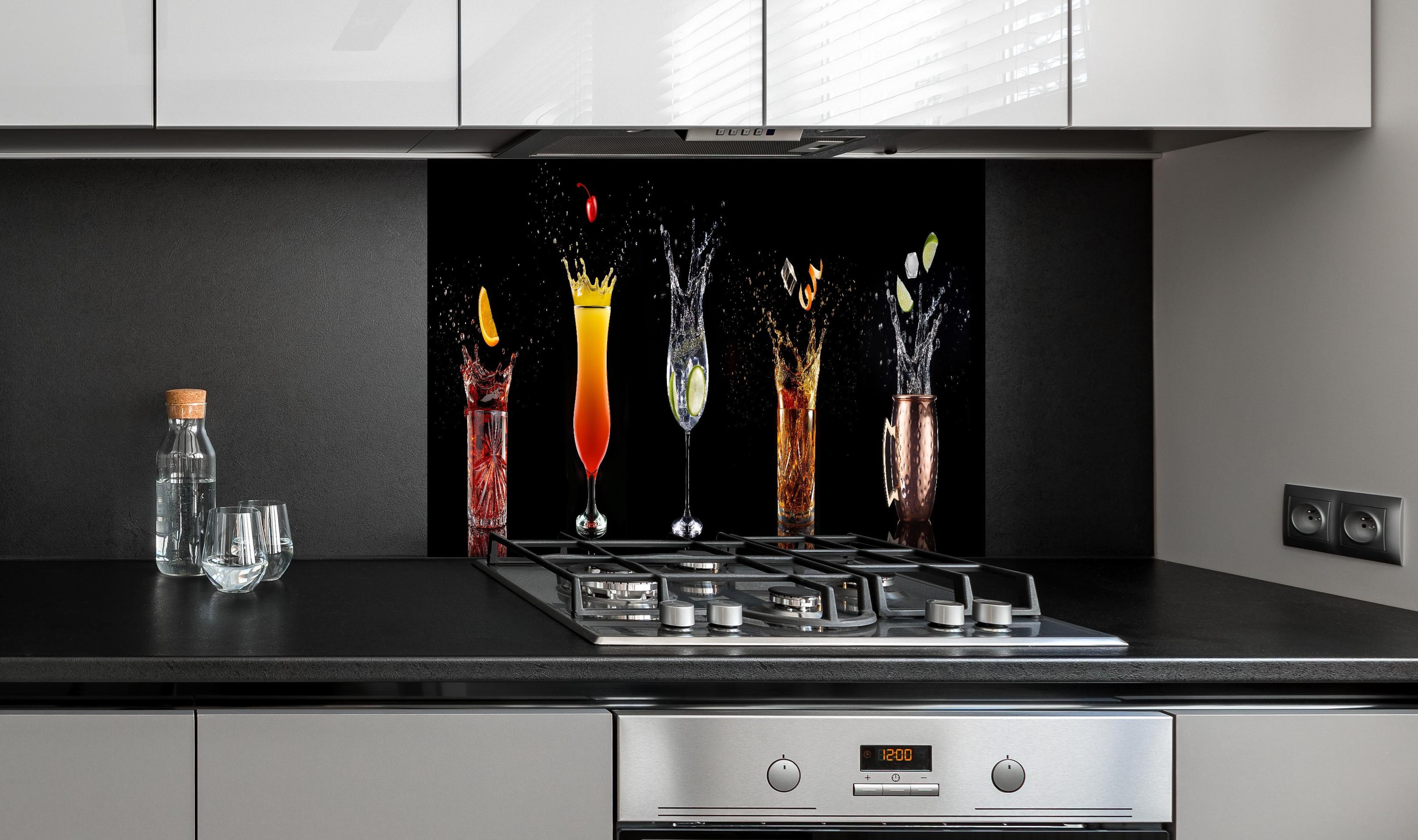 Spritzschutz - Splash-Effekt mit Cocktails auf Schwarz hinter einem Cerankochfeld zwischen Holz-Kochutensilien