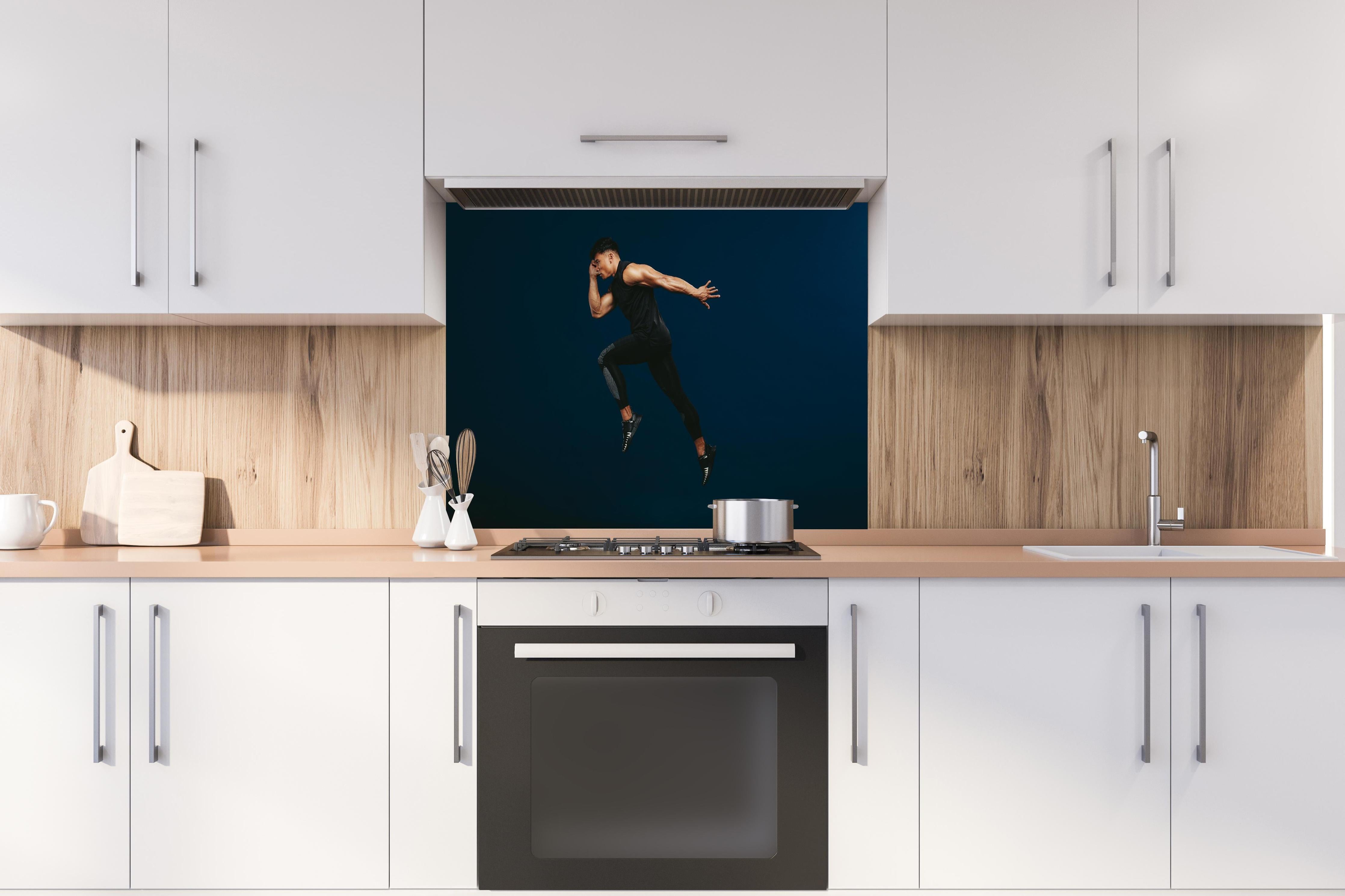 Spritzschutz - Sportler bei einem Sprung hinter einem Cerankochfeld zwischen Holz-Kochutensilien