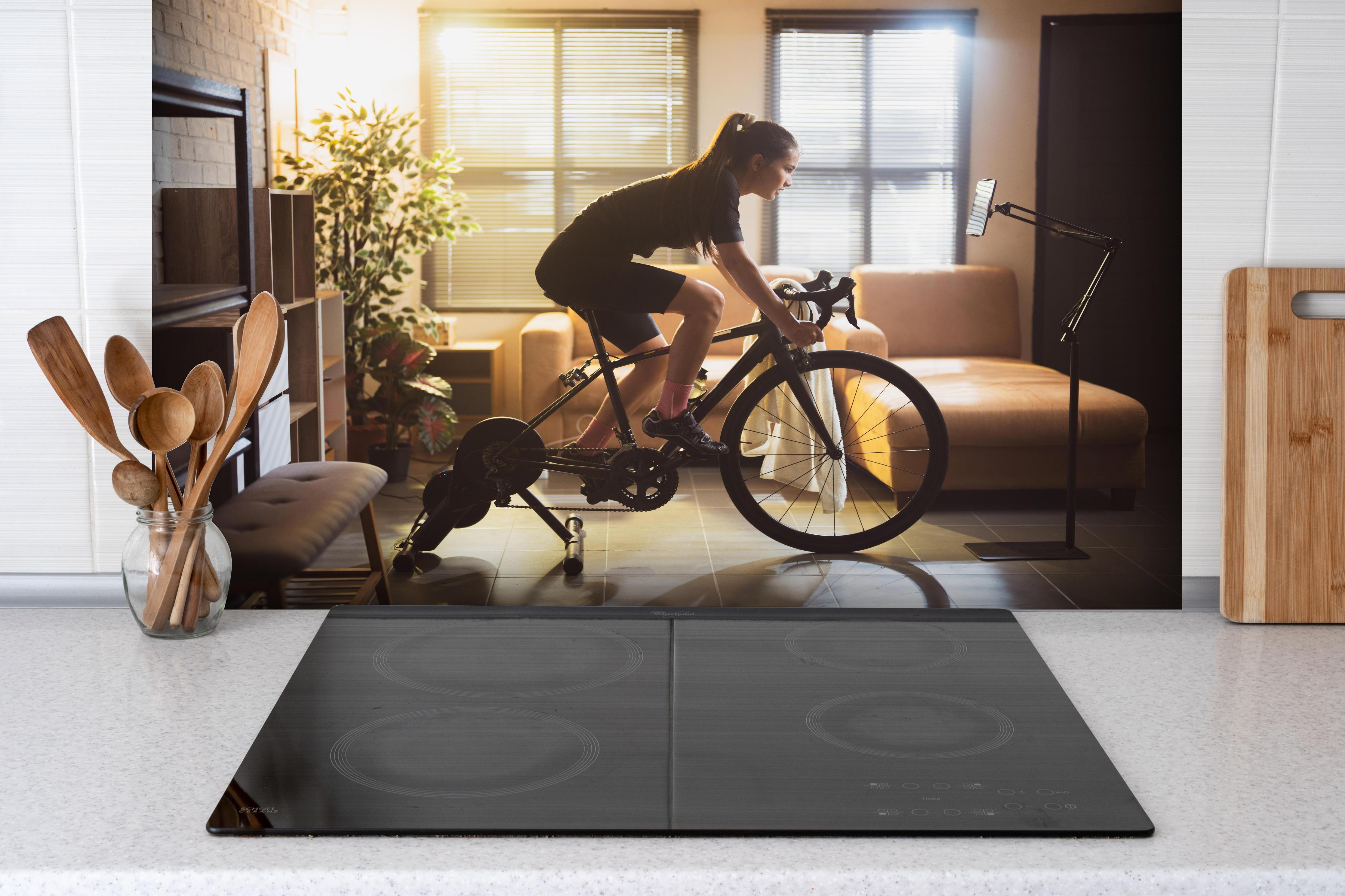 Spritzschutz - Sportliche Radfahrerin hinter einem Cerankochfeld zwischen Holz-Kochutensilien