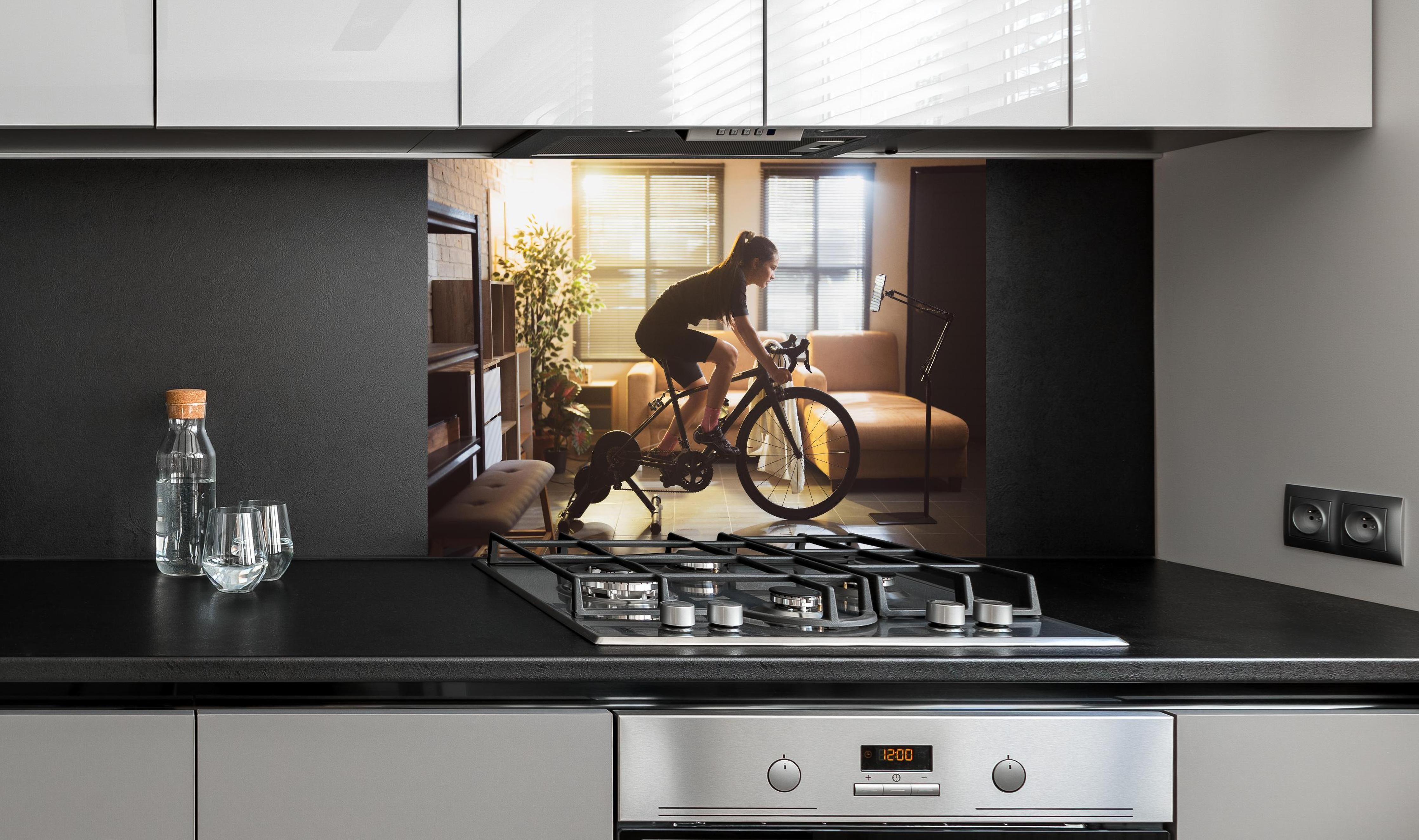 Spritzschutz - Sportliche Radfahrerin hinter einem Cerankochfeld zwischen Holz-Kochutensilien