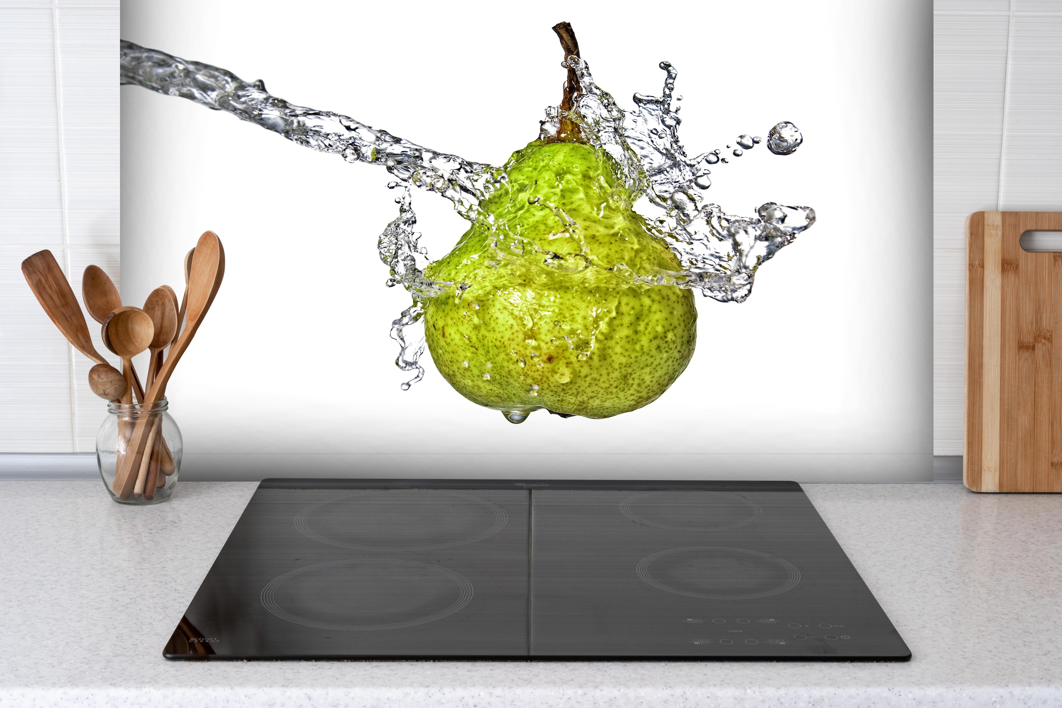 Spritzschutz - Spritzige Birne hinter einem Cerankochfeld zwischen Holz-Kochutensilien