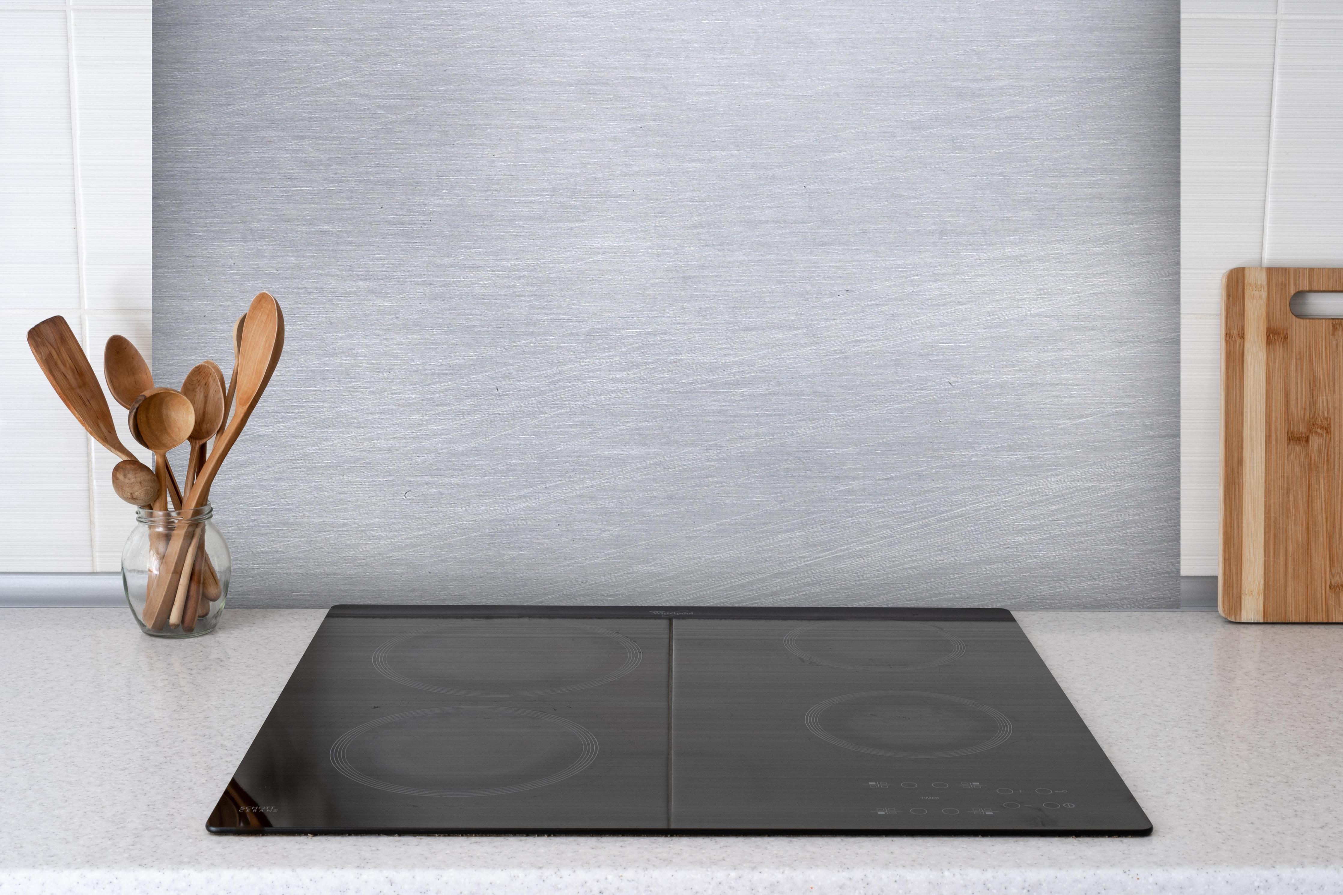 Spritzschutz - Gebürsteter Stahl hinter einem Cerankochfeld zwischen Holz-Kochutensilien