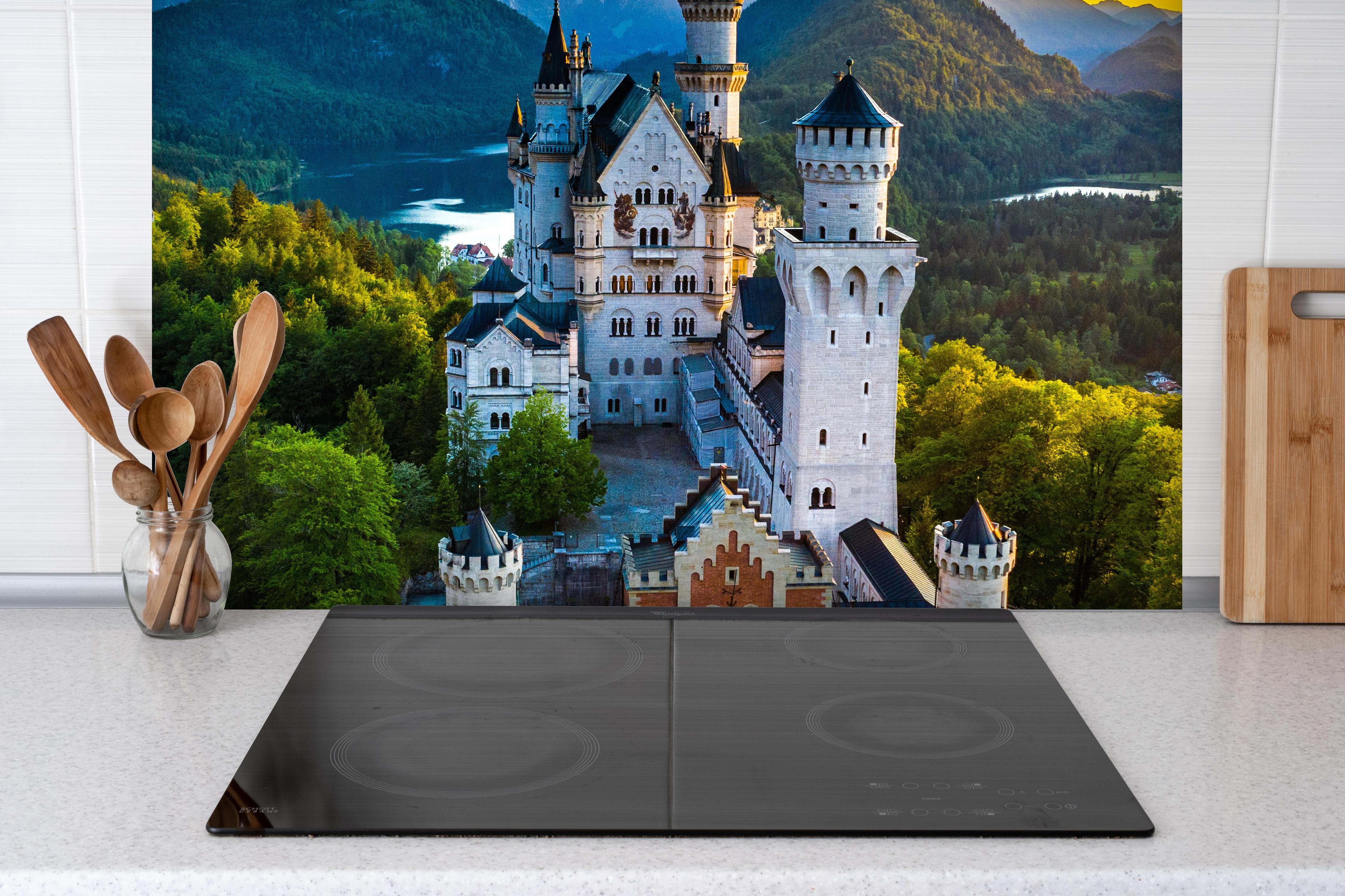 Spritzschutz - glanzvolles Märchenschloss Neuschwanstein hinter einem Cerankochfeld zwischen Holz-Kochutensilien