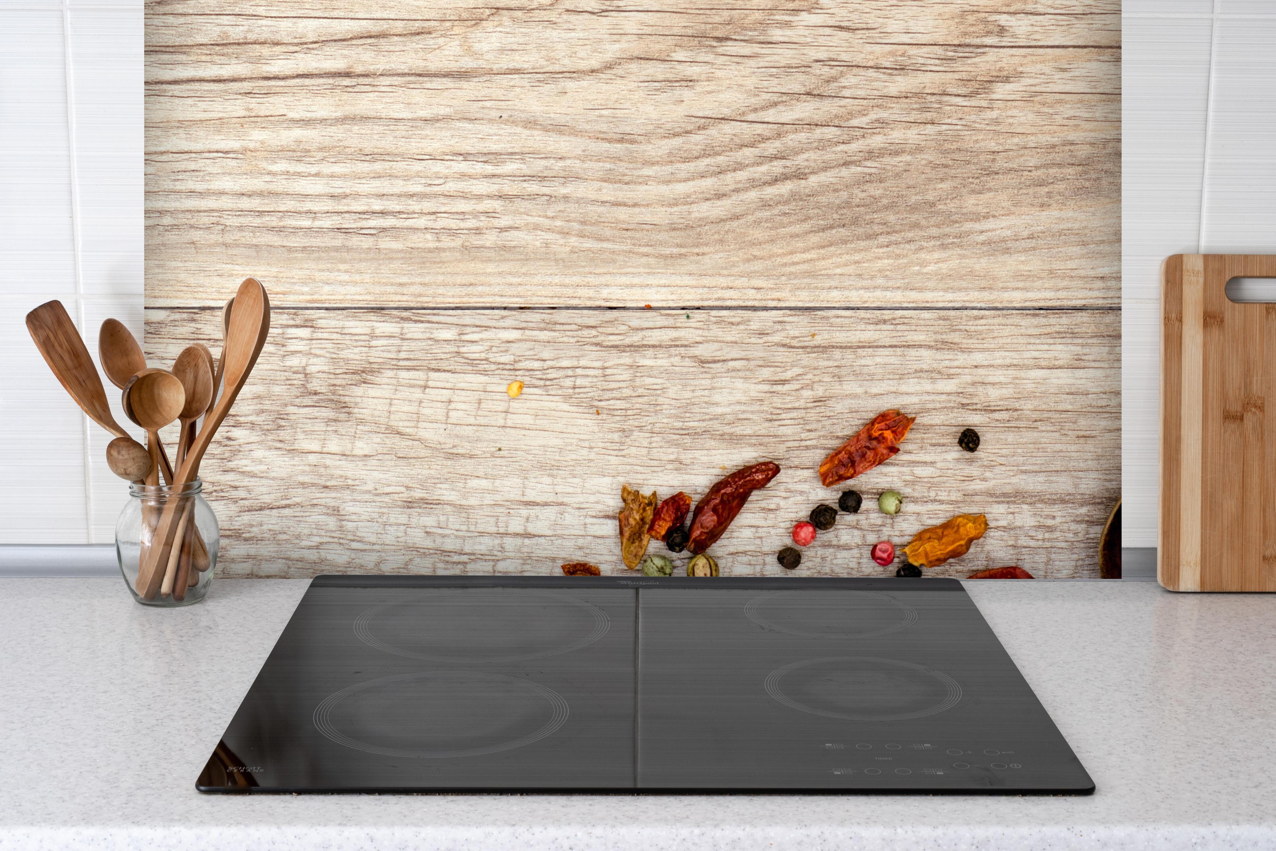 Spritzschutz - trockenes Gemüse durcheinander auf Holz hinter einem Cerankochfeld zwischen Holz-Kochutensilien