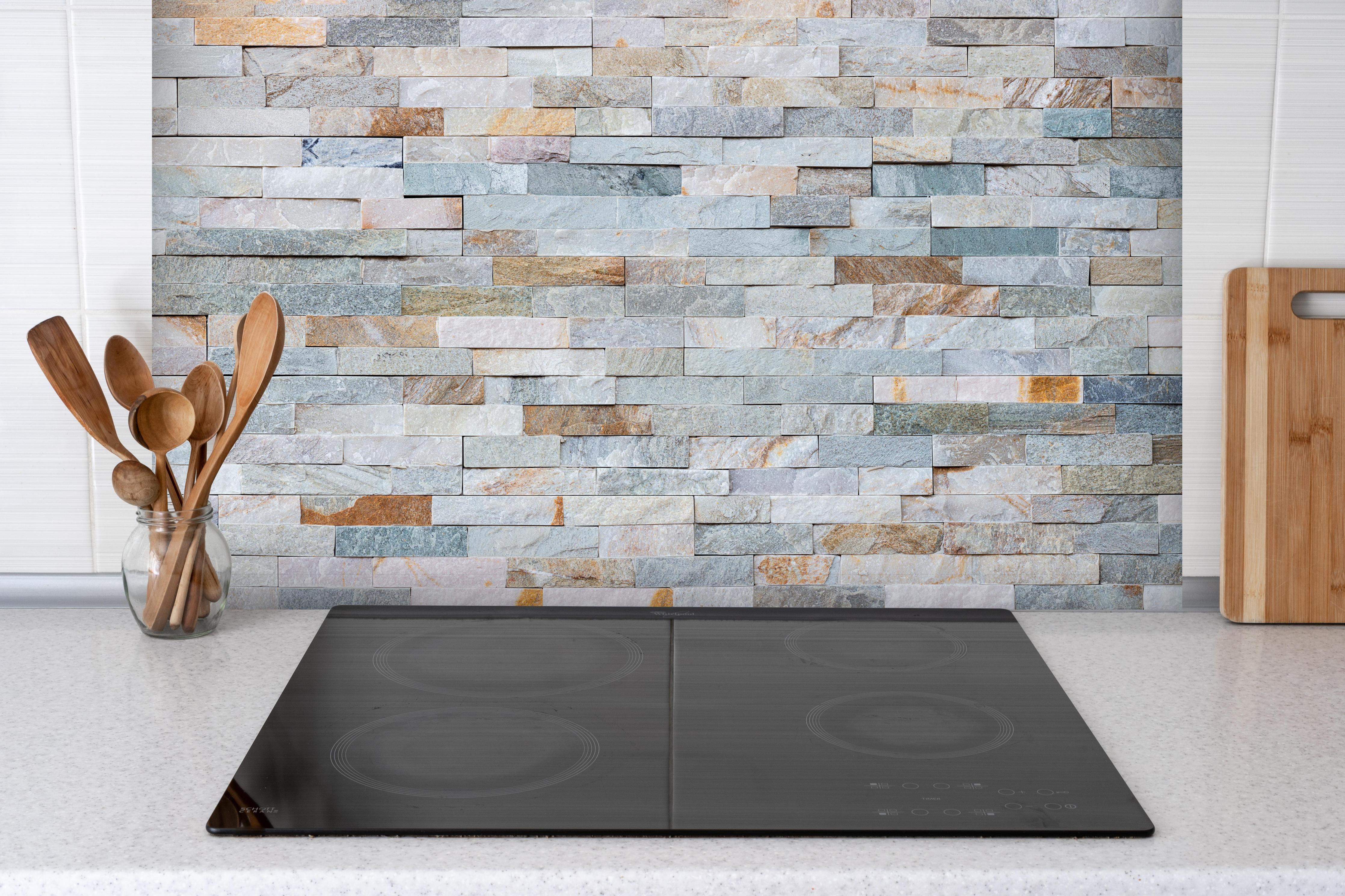 Spritzschutz - Abstrakte Steinwandmuster hinter einem Cerankochfeld zwischen Holz-Kochutensilien
