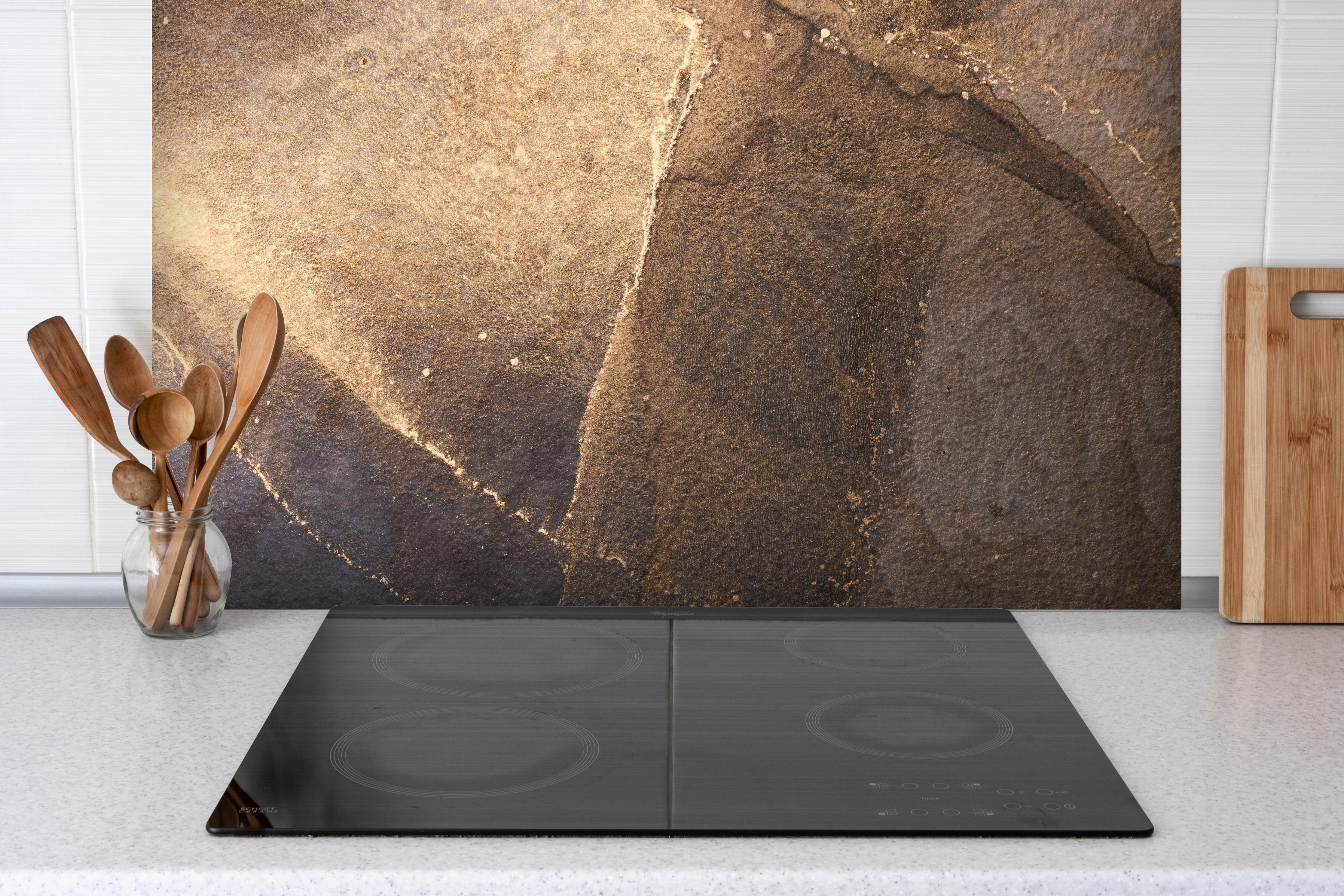 Spritzschutz - Abstrakte dunkle Tinte mit Goldelementen hinter einem Cerankochfeld zwischen Holz-Kochutensilien