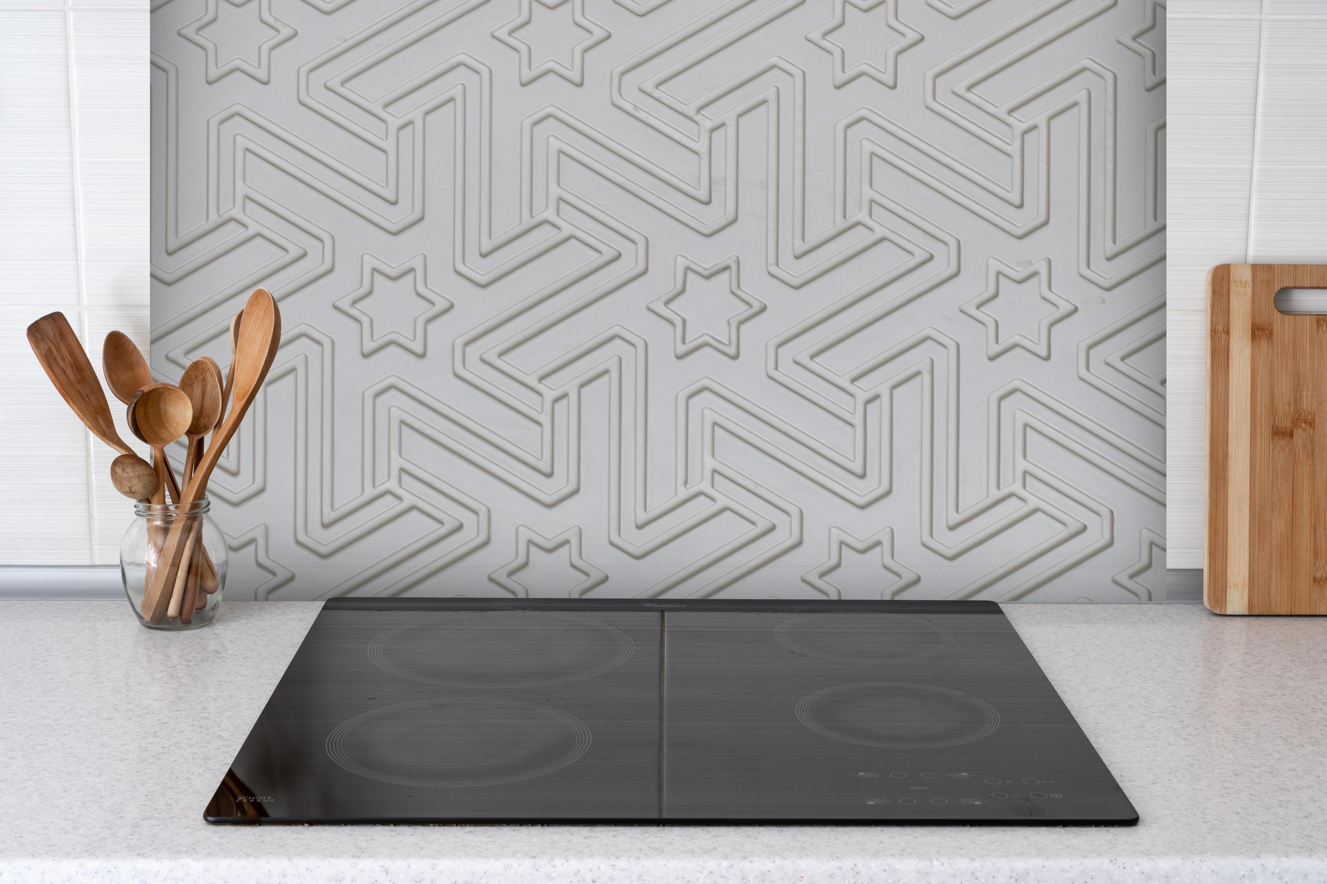 Spritzschutz - Abstraktes geometrisches Fliesenmuster hinter einem Cerankochfeld zwischen Holz-Kochutensilien