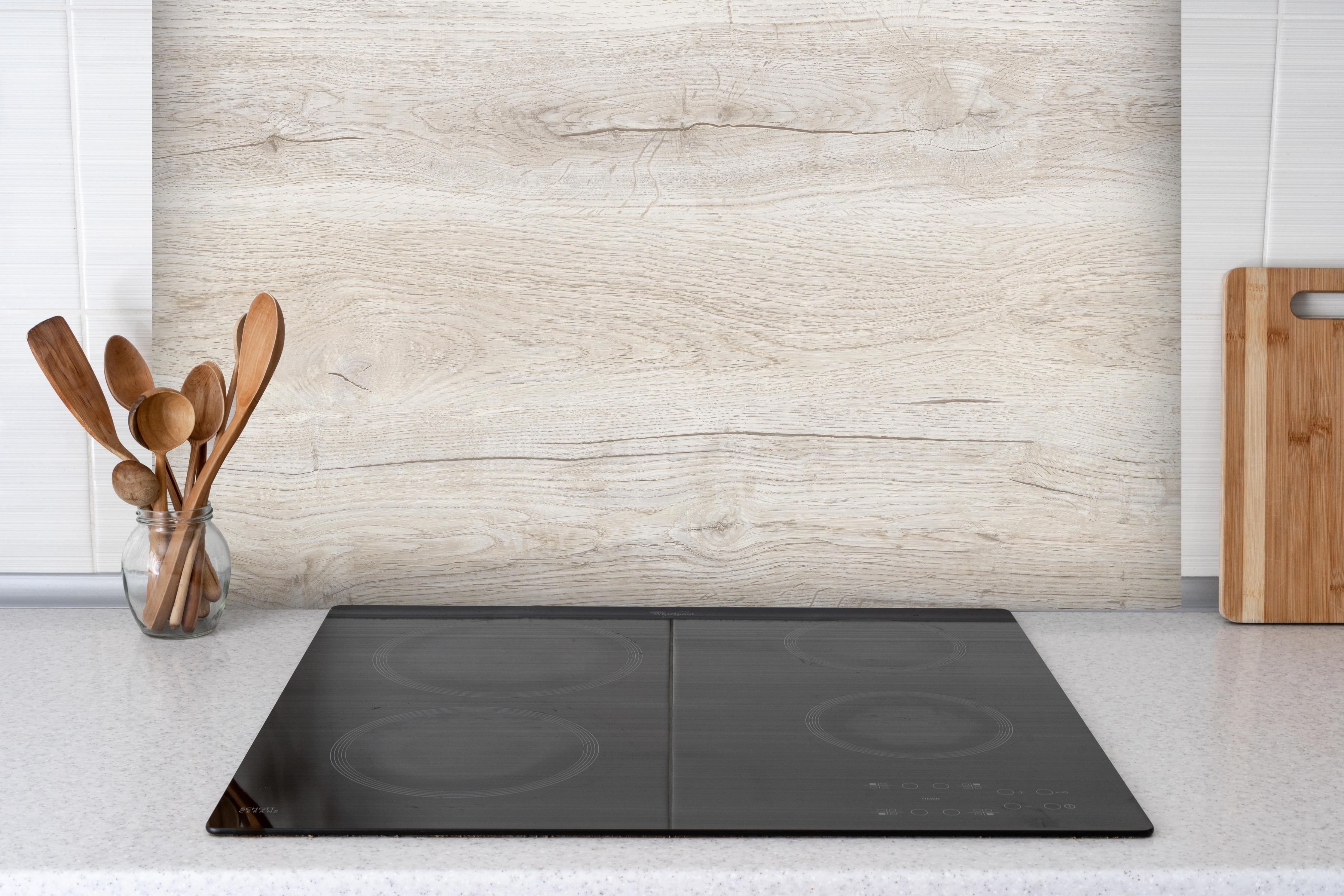 Spritzschutz - Ahornholzplatte hinter einem Cerankochfeld zwischen Holz-Kochutensilien