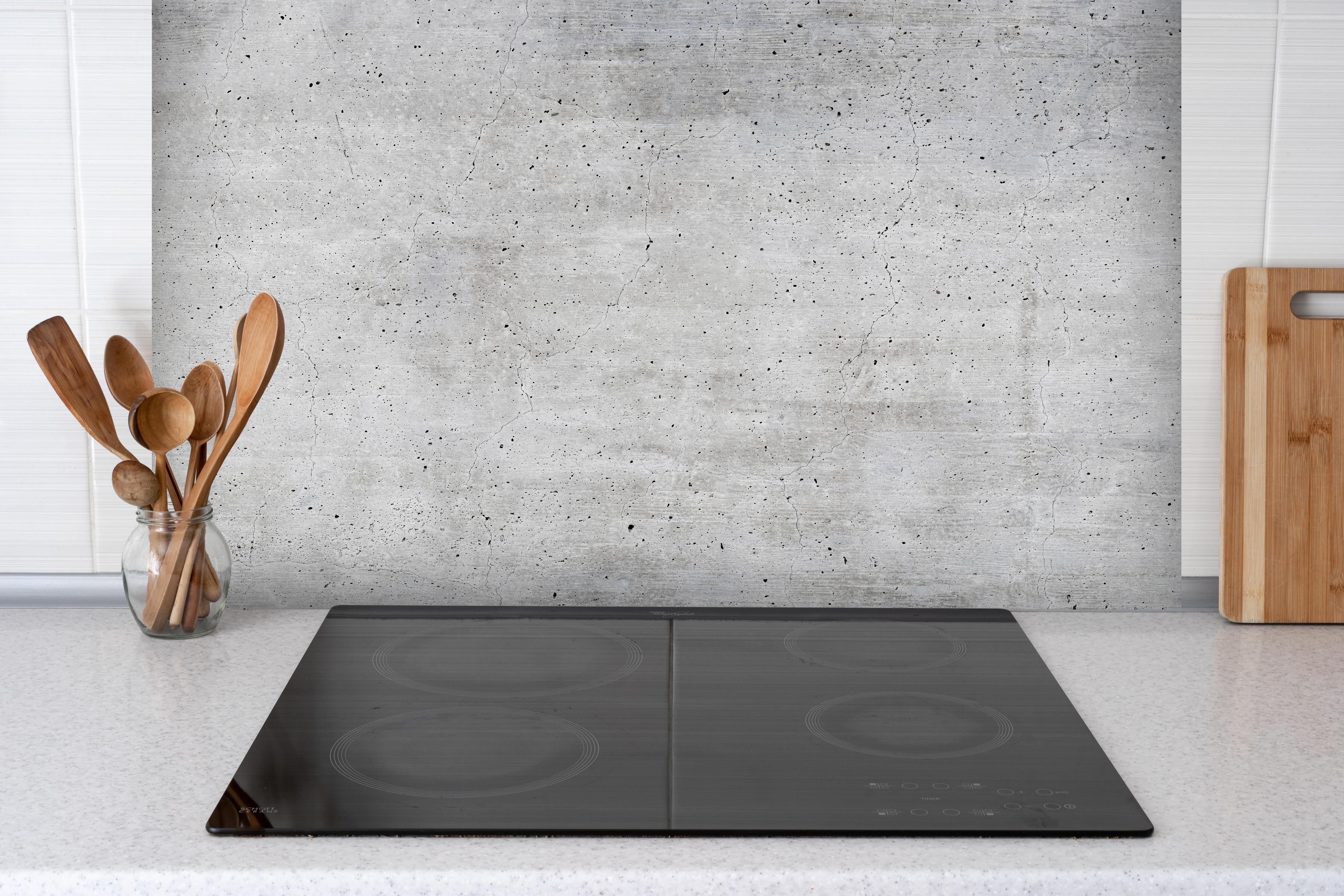 Spritzschutz - Alte gräuliche Betonmauer hinter einem Cerankochfeld zwischen Holz-Kochutensilien