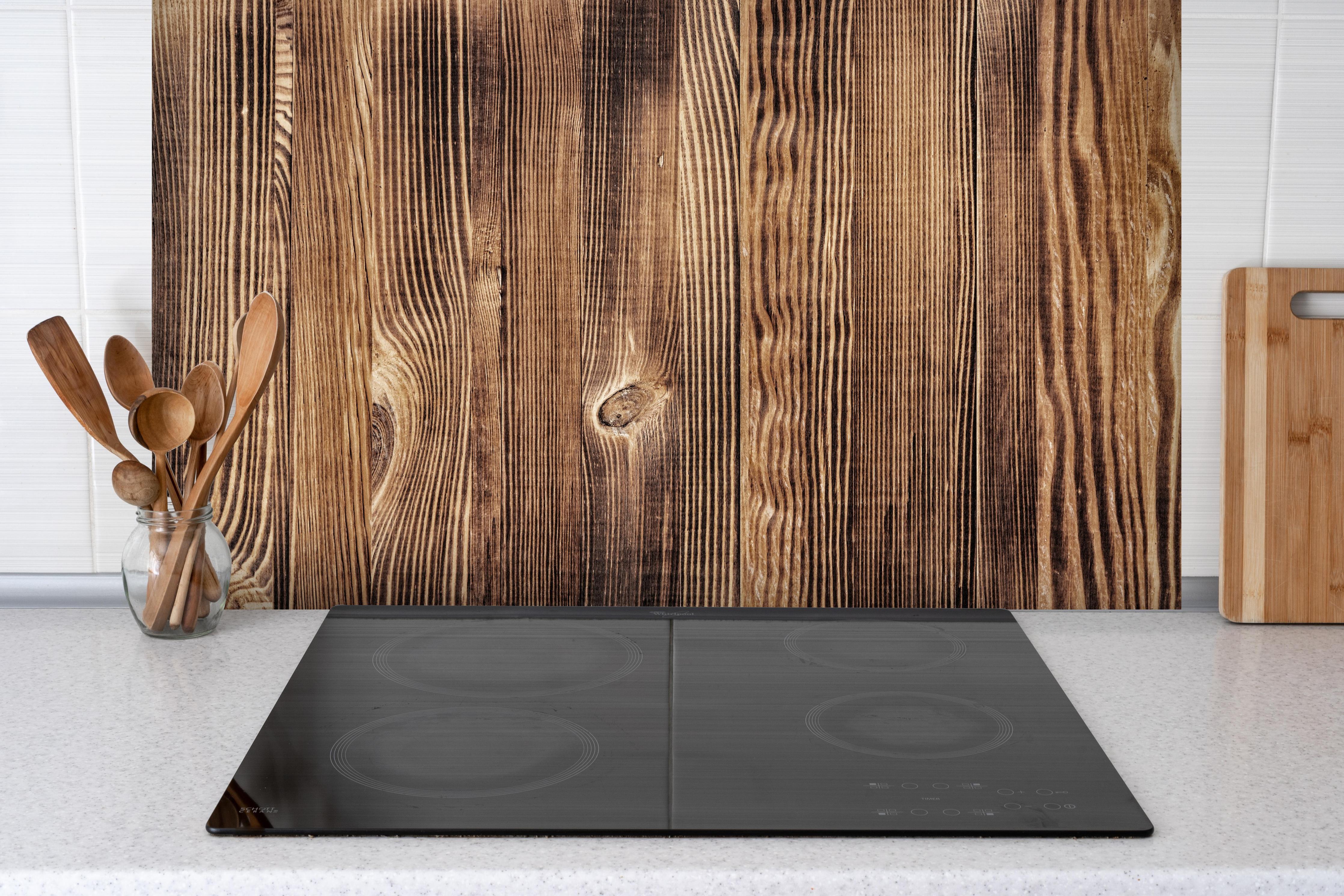 Spritzschutz - Angebrannte Naturholzplatte hinter einem Cerankochfeld zwischen Holz-Kochutensilien