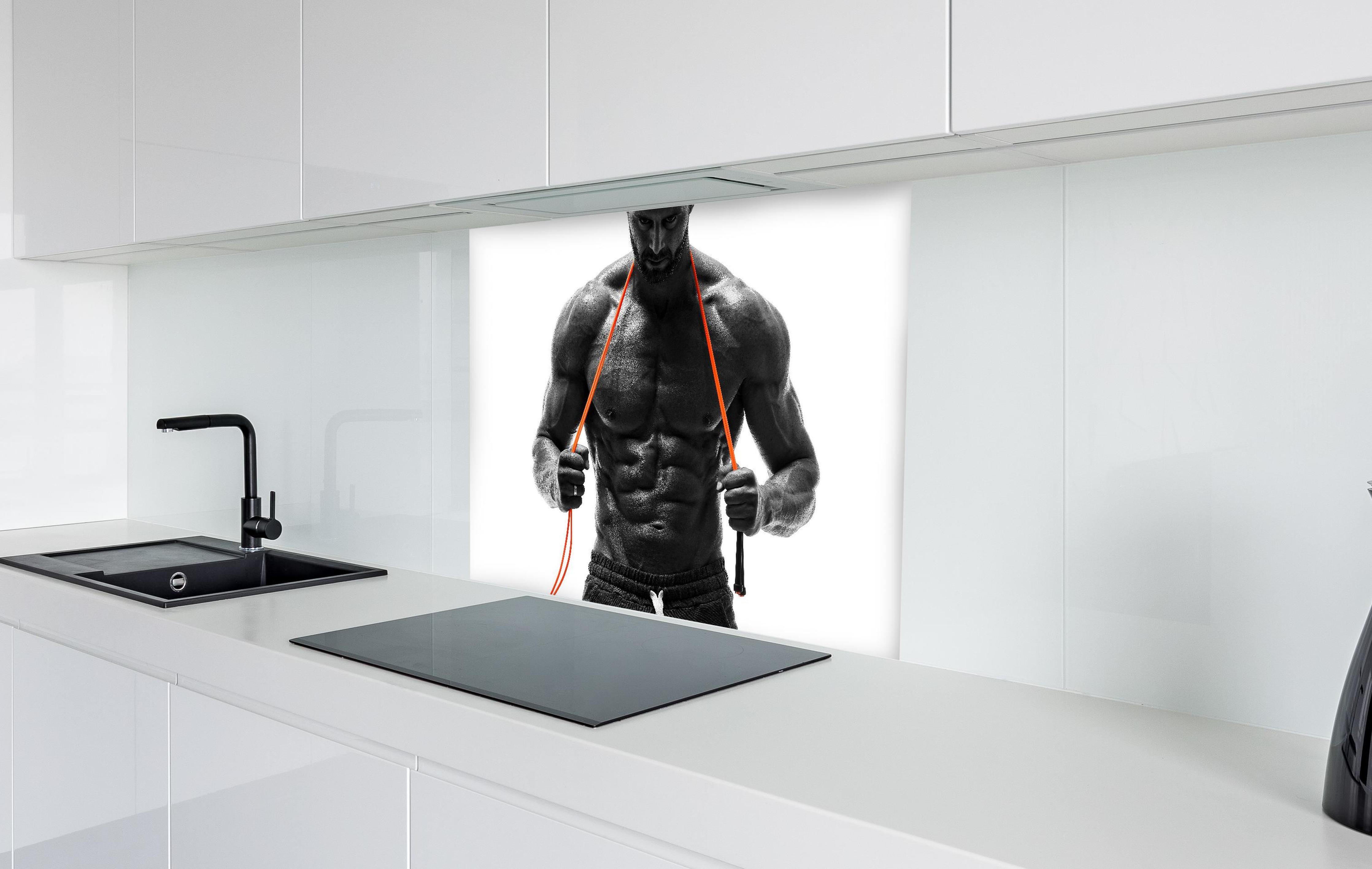 Spritzschutz - Athletischer Mann posiert mit Sprungseil in weißer Hochglanz-Küche hinter einem Cerankochfeld
