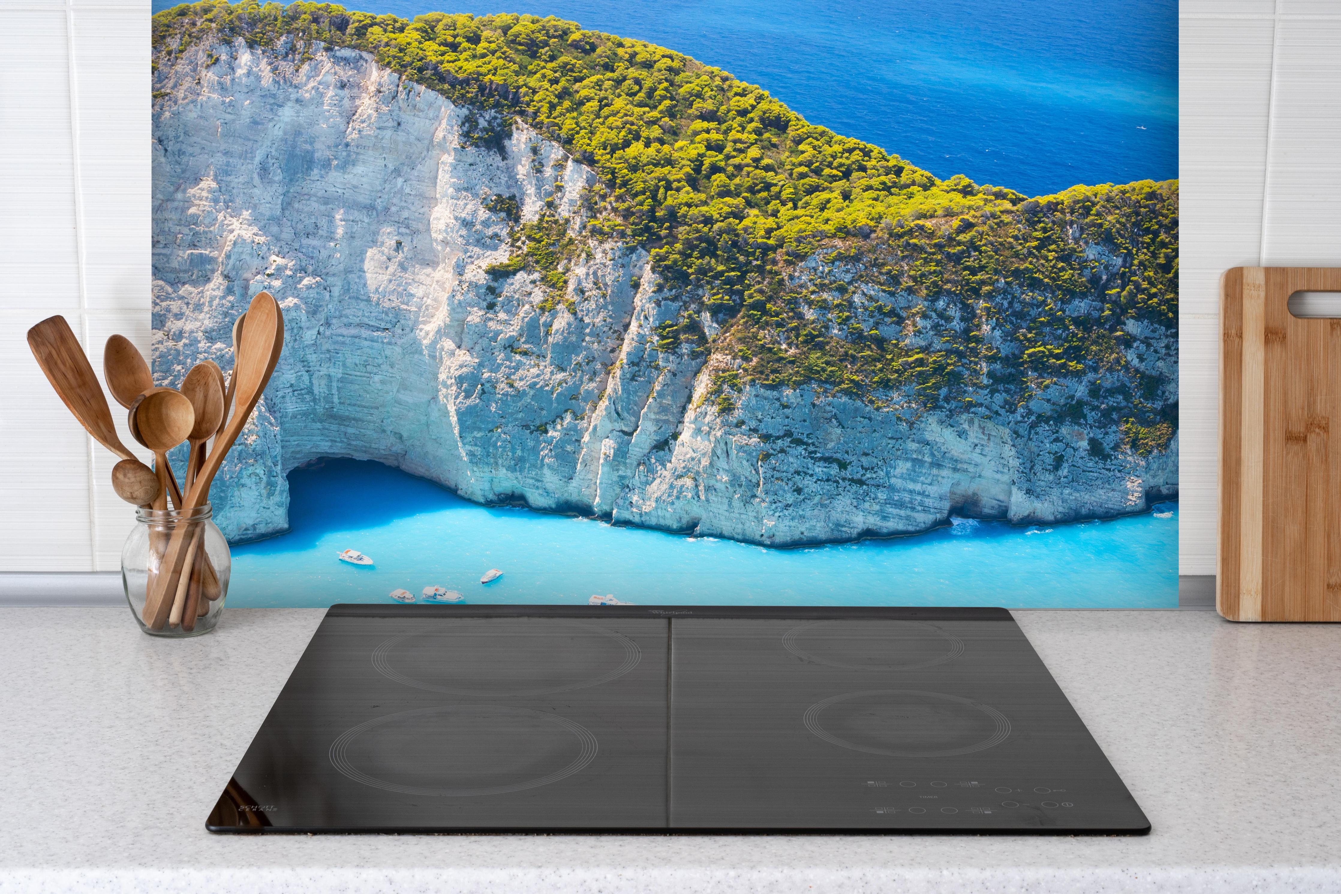 Spritzschutz - Ausblick auf Zakynthos Bucht hinter einem Cerankochfeld zwischen Holz-Kochutensilien