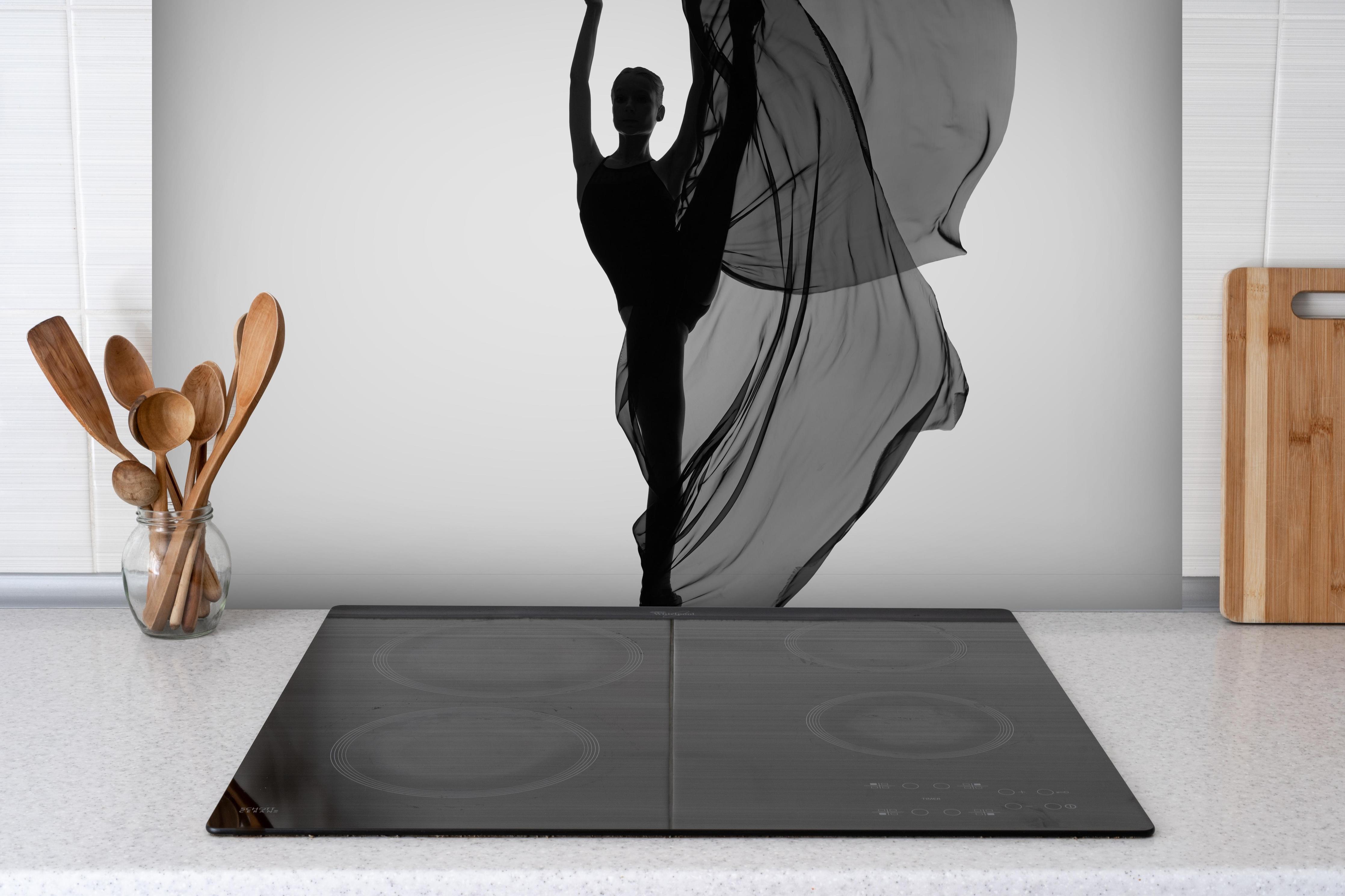 Spritzschutz - Ballerina tanzt mit schwarzem Tuch hinter einem Cerankochfeld zwischen Holz-Kochutensilien