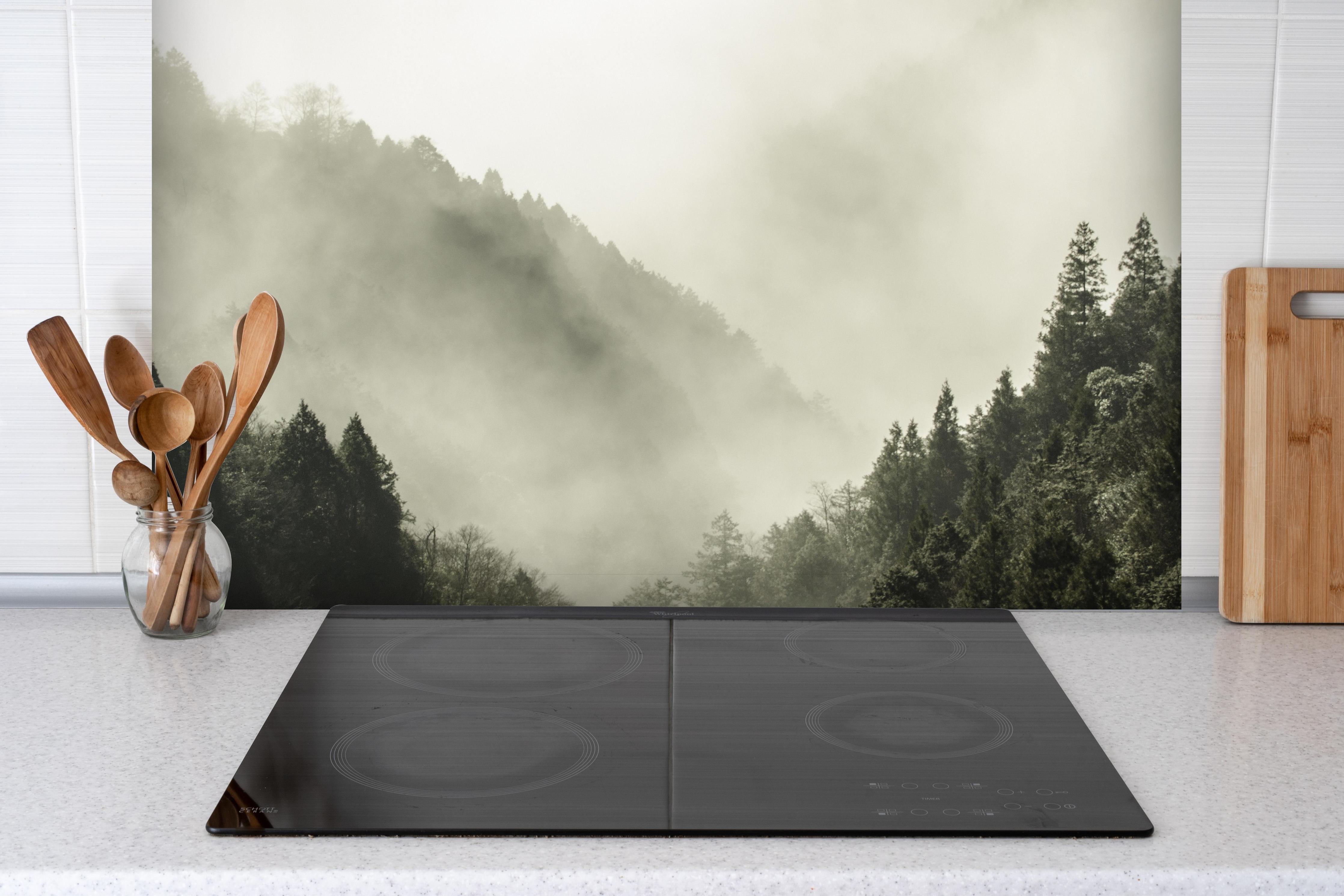 Spritzschutz - Berg bedeckt in Nebel und Wolken hinter einem Cerankochfeld zwischen Holz-Kochutensilien