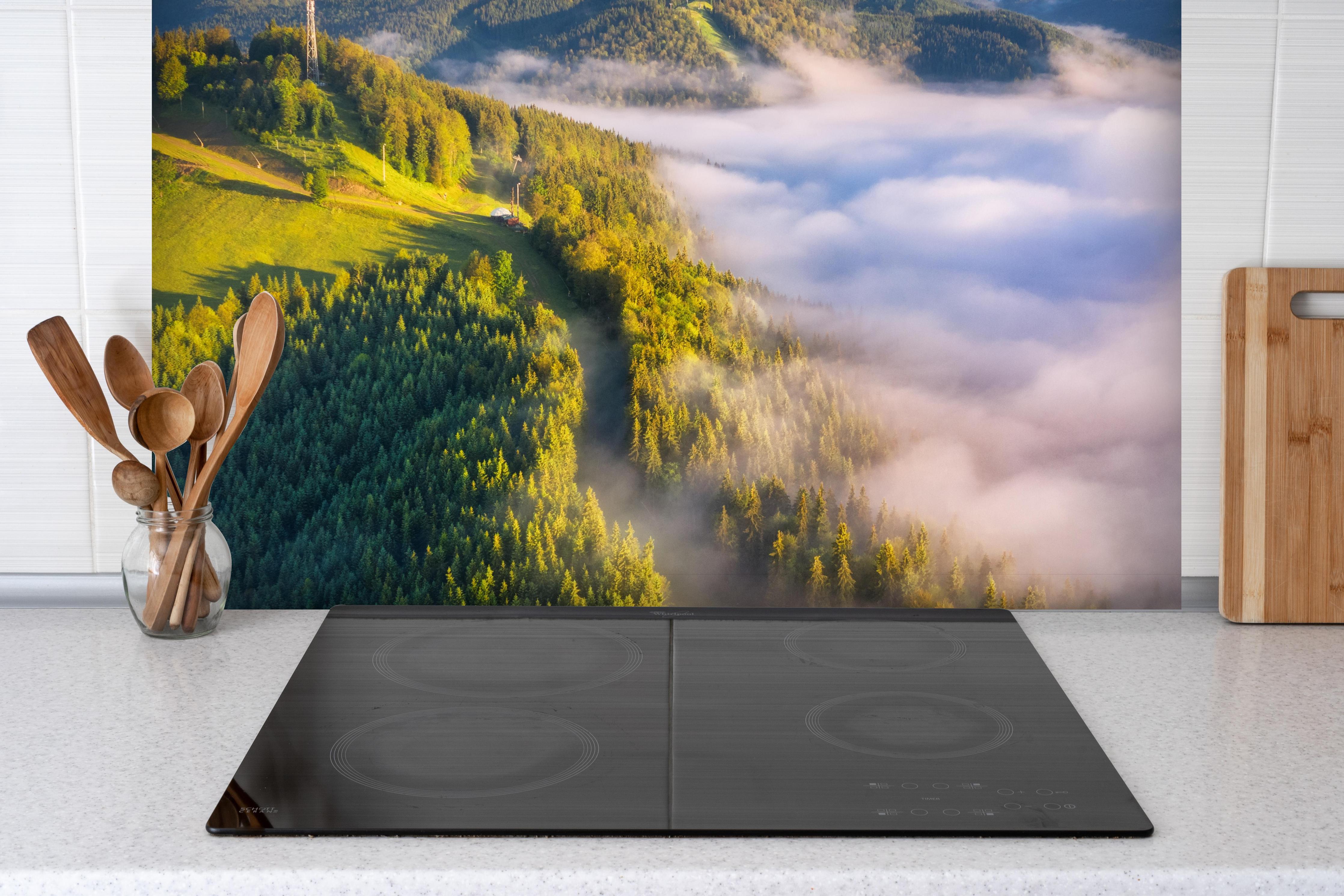 Spritzschutz - Berge in Wolken bei Sonnenaufgang im Sommer hinter einem Cerankochfeld zwischen Holz-Kochutensilien