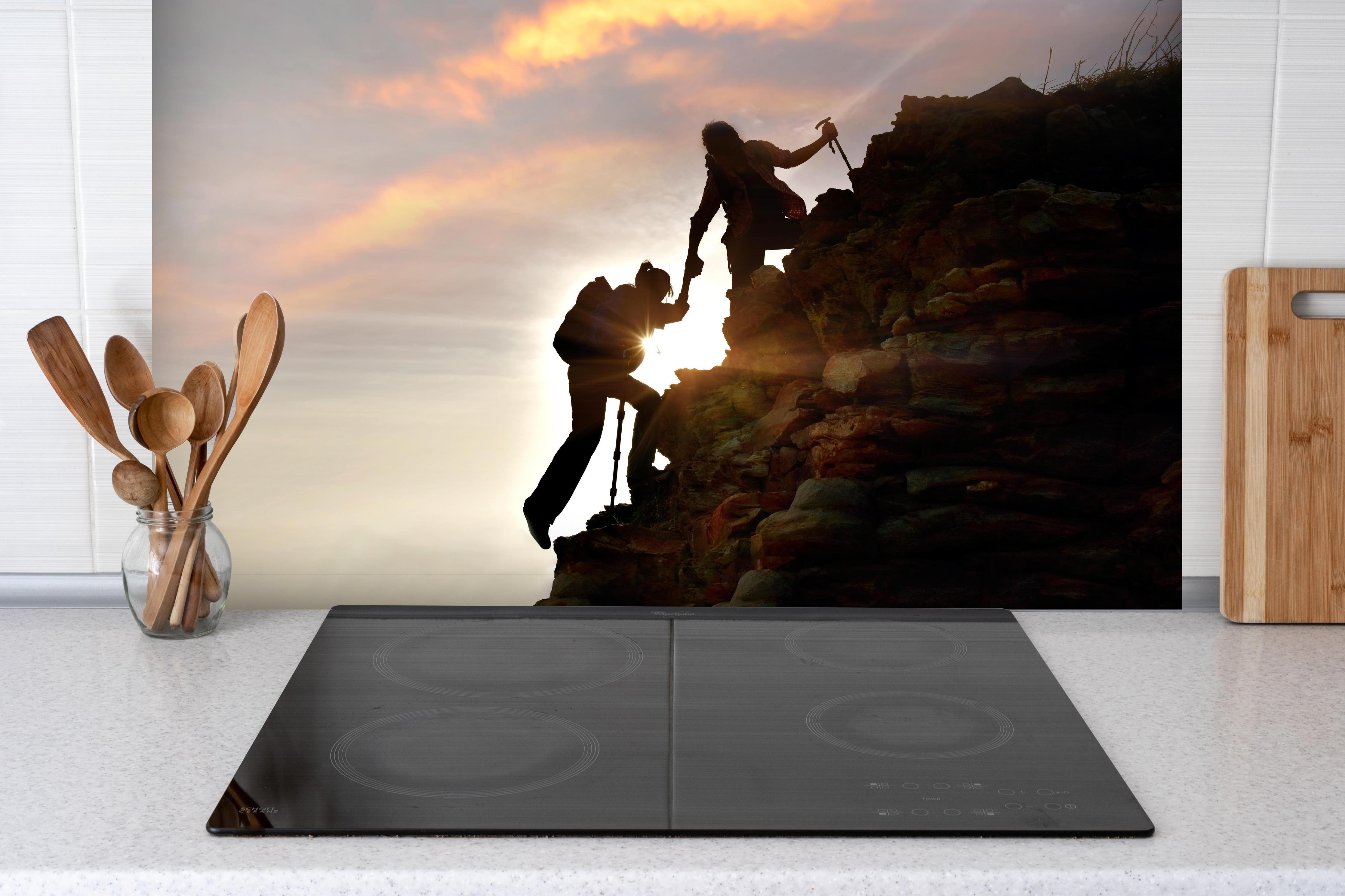 Spritzschutz - Bergsteiger bei Sonnenuntergang hinter einem Cerankochfeld zwischen Holz-Kochutensilien