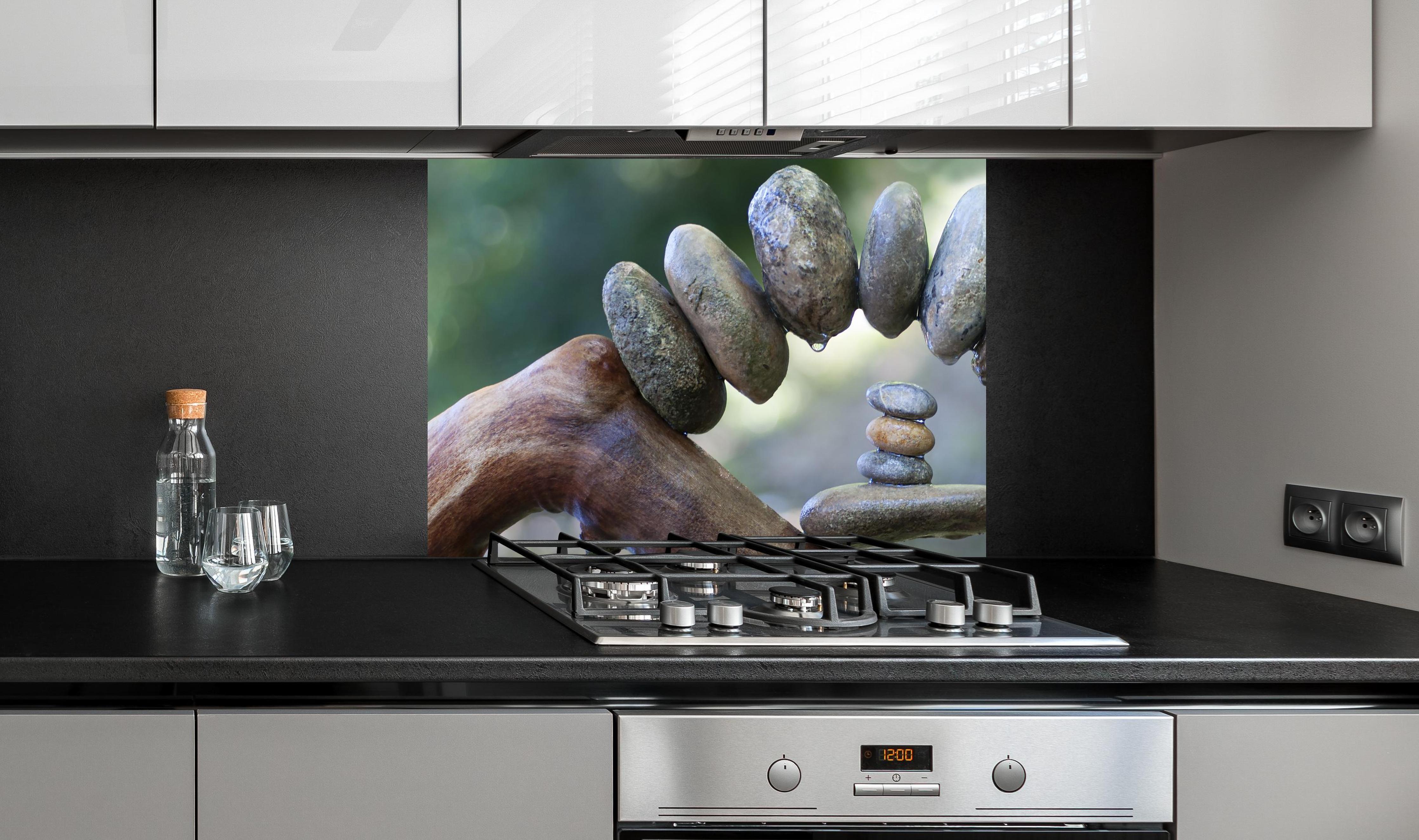 Spritzschutz - Bogen aus Steinen und Holz auf dem Wasser an edler Anthrazit-Wand hinter silbernem Gasherd