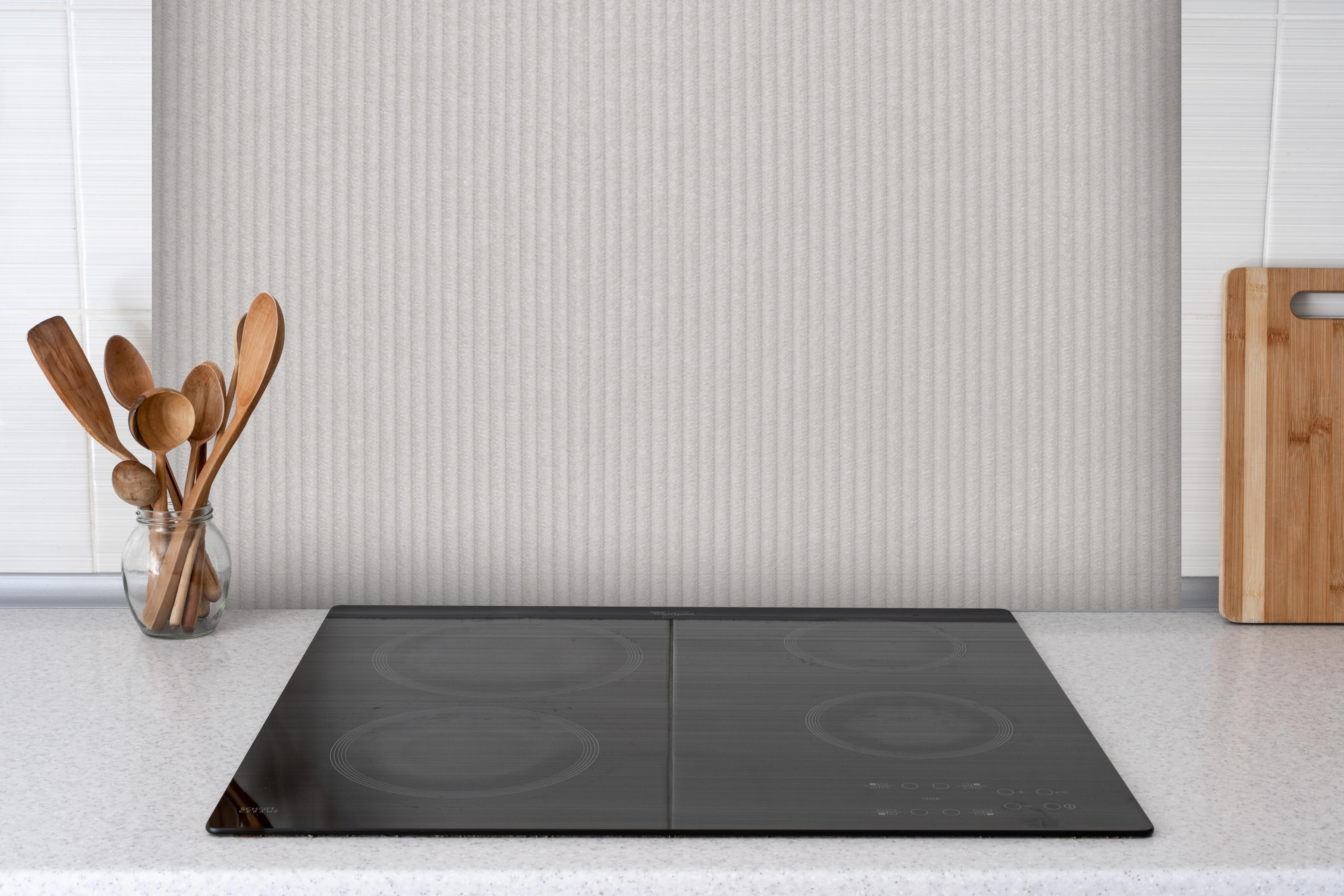 Spritzschutz - Bräunliches Kord Textil hinter einem Cerankochfeld zwischen Holz-Kochutensilien