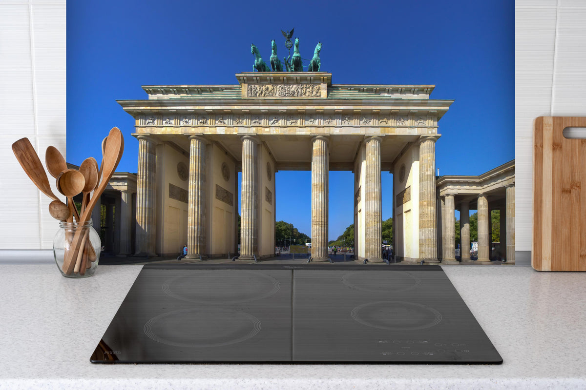 Spritzschutz - Brandenburger Tor in Berlin bei Tag hinter einem Cerankochfeld zwischen Holz-Kochutensilien
