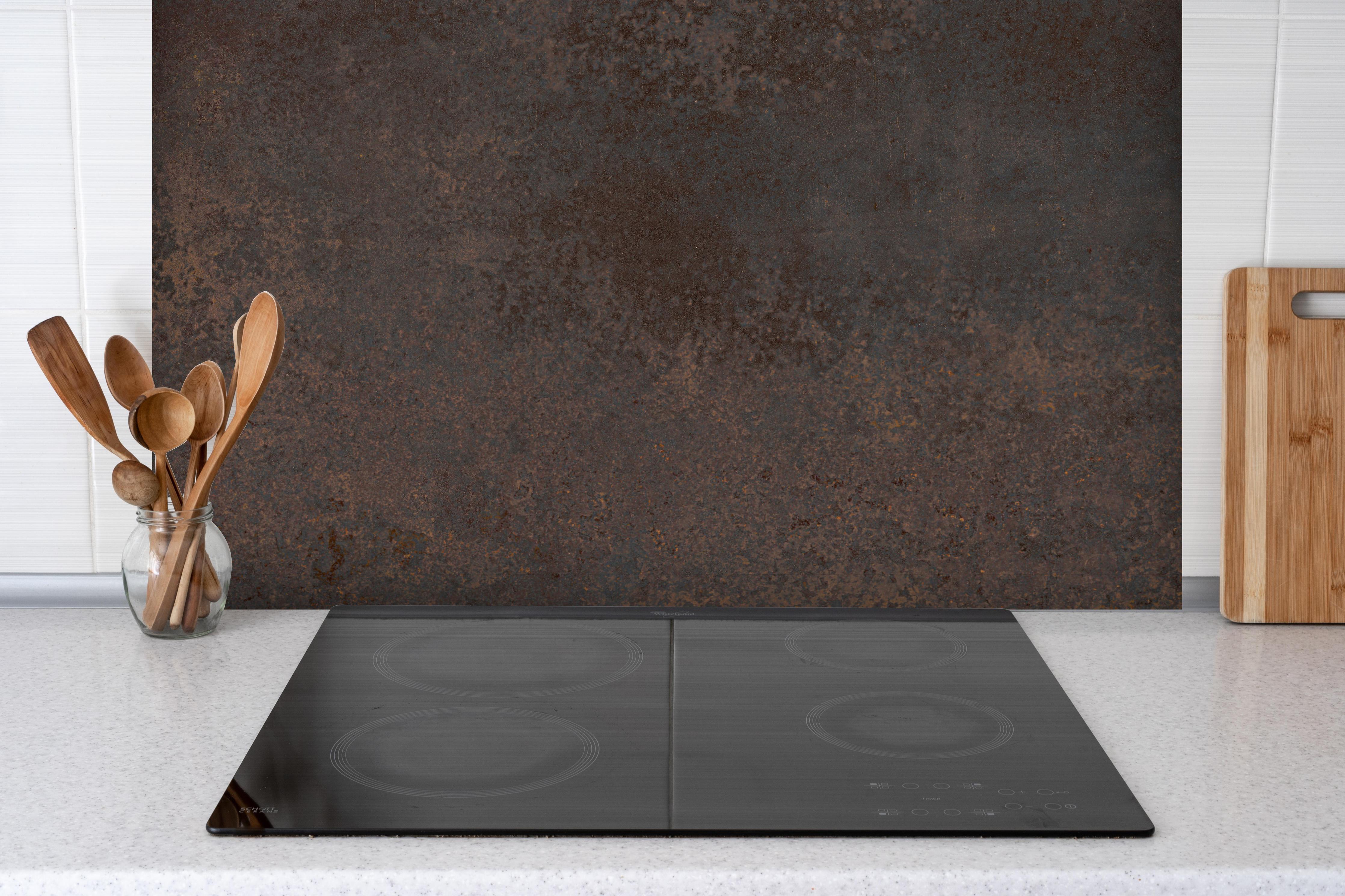 Spritzschutz - Braun-Grauer Zement hinter einem Cerankochfeld zwischen Holz-Kochutensilien