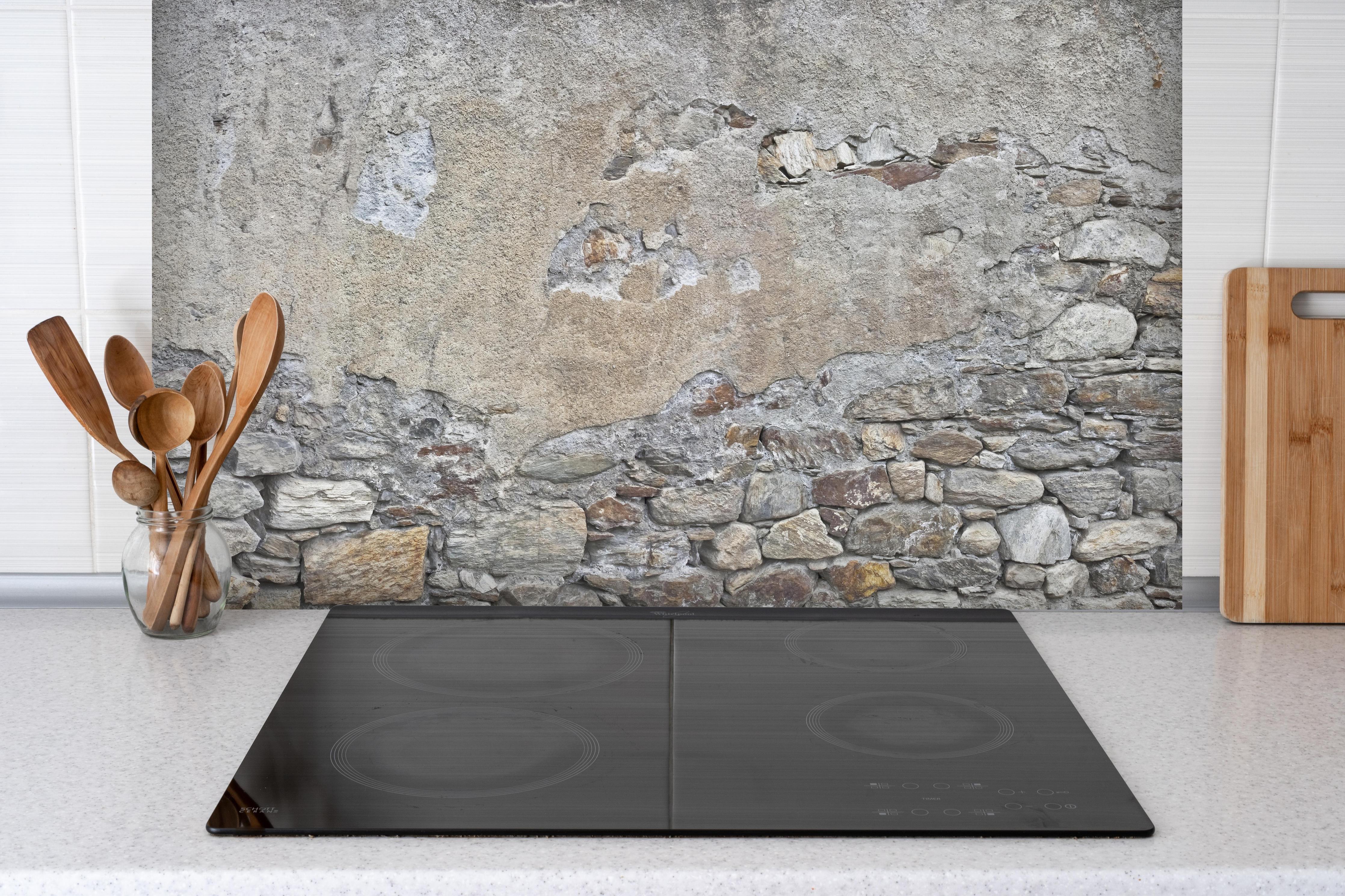 Spritzschutz - Bröckelnde Hausmauer in Südtirol hinter einem Cerankochfeld zwischen Holz-Kochutensilien