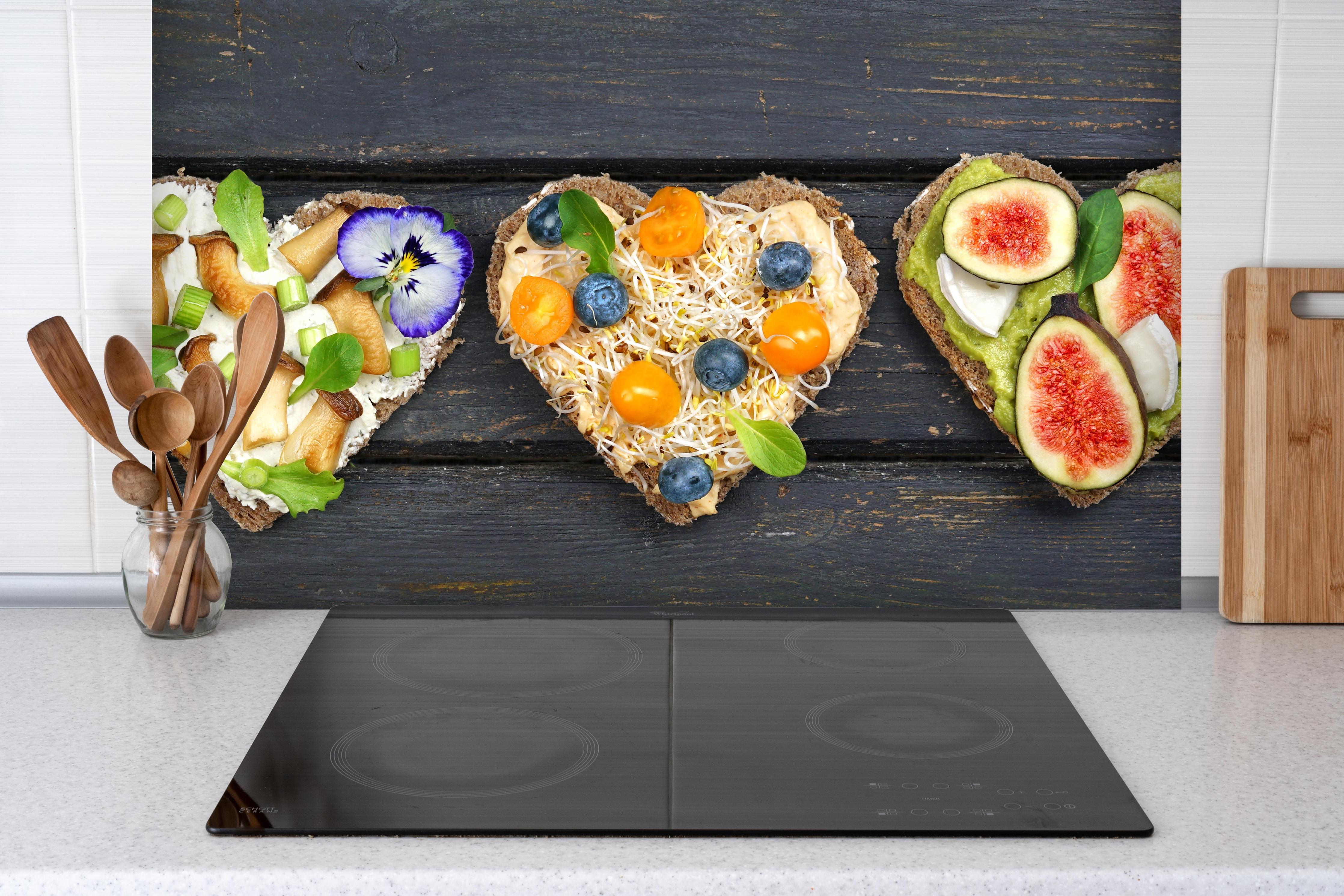 Spritzschutz - Bunt belegte Brote hinter einem Cerankochfeld zwischen Holz-Kochutensilien