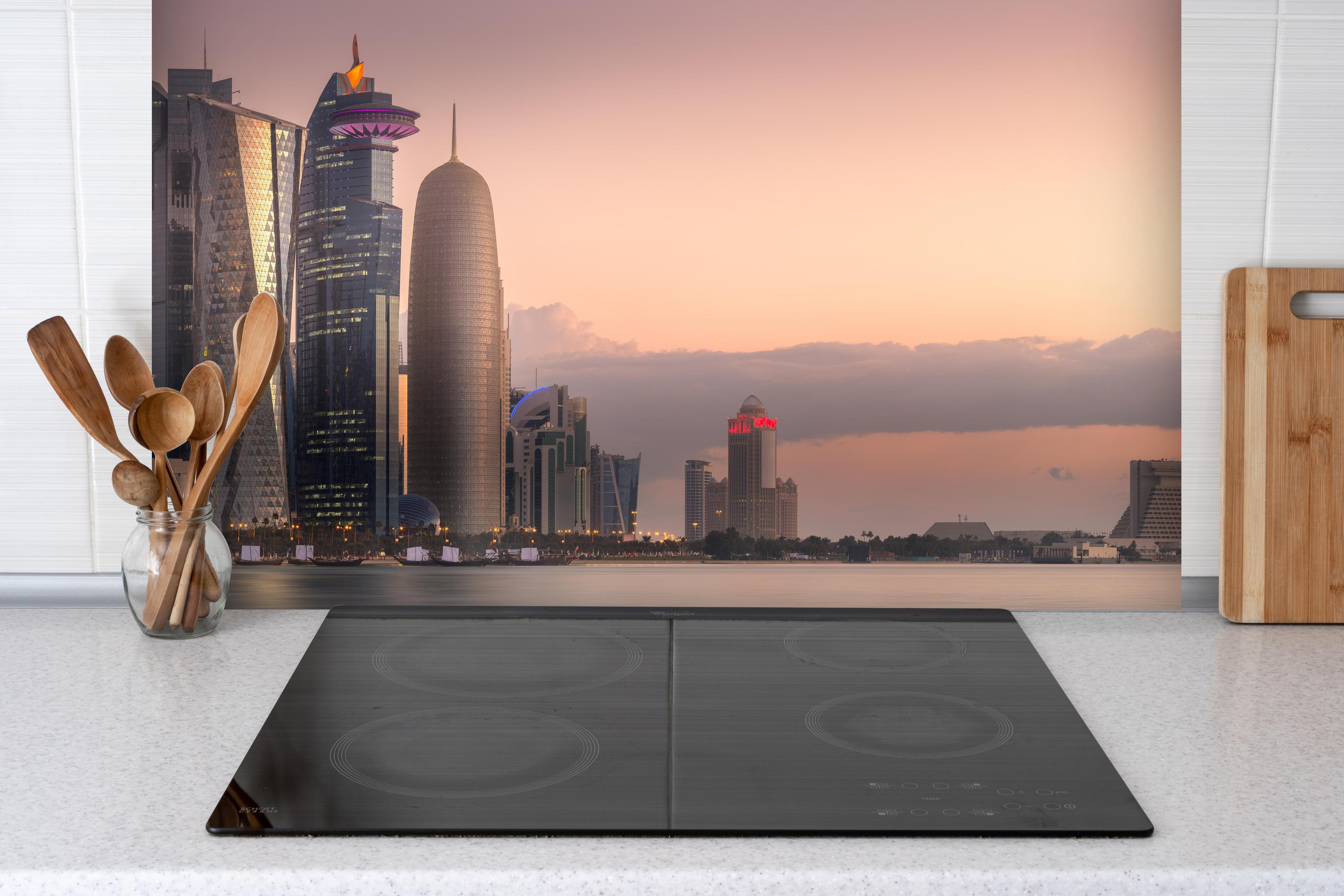 Spritzschutz - Die Skyline von West Bay und Doha City hinter einem Cerankochfeld zwischen Holz-Kochutensilien