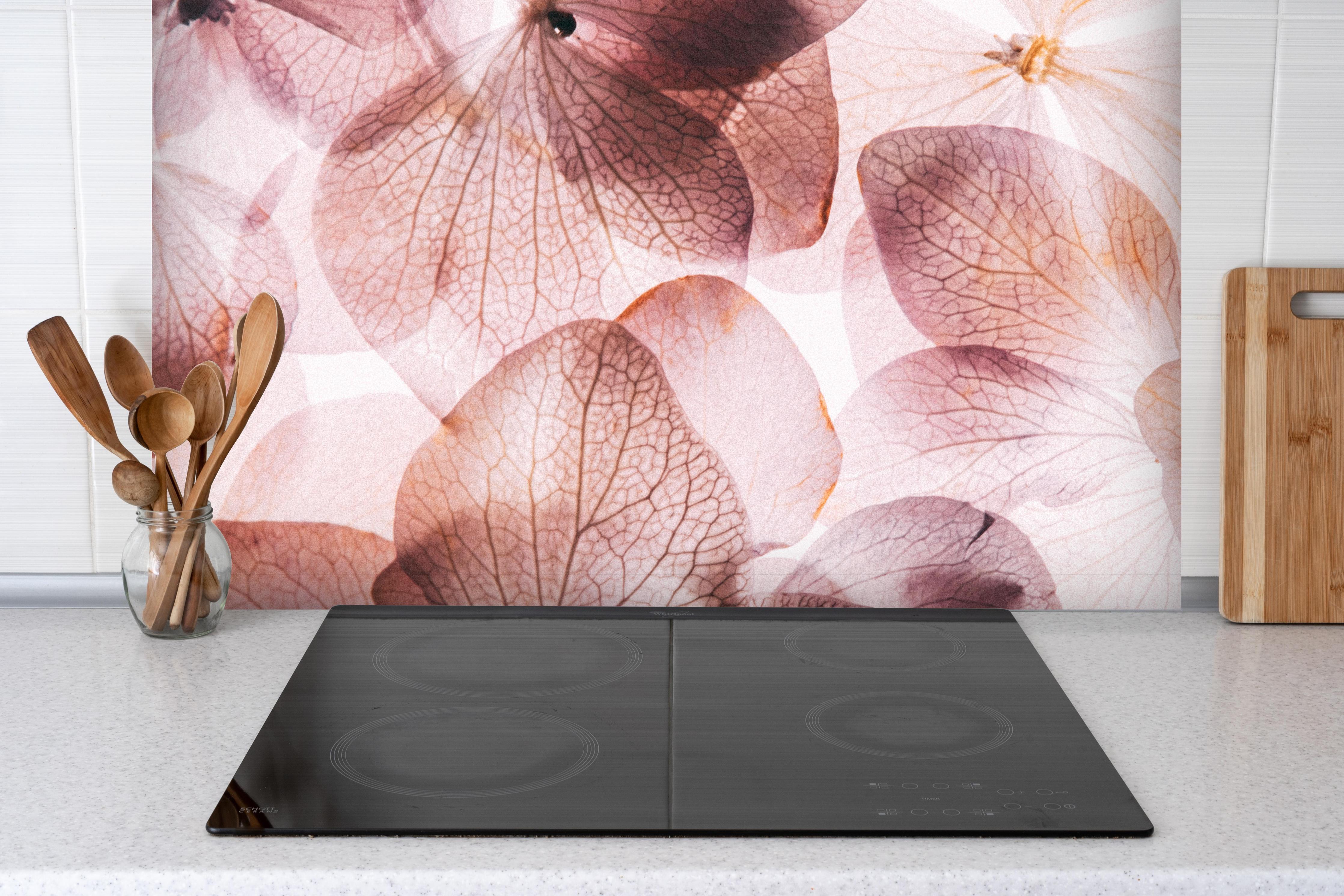 Spritzschutz - Dünne rosafarbige Hortensienblüten hinter einem Cerankochfeld zwischen Holz-Kochutensilien