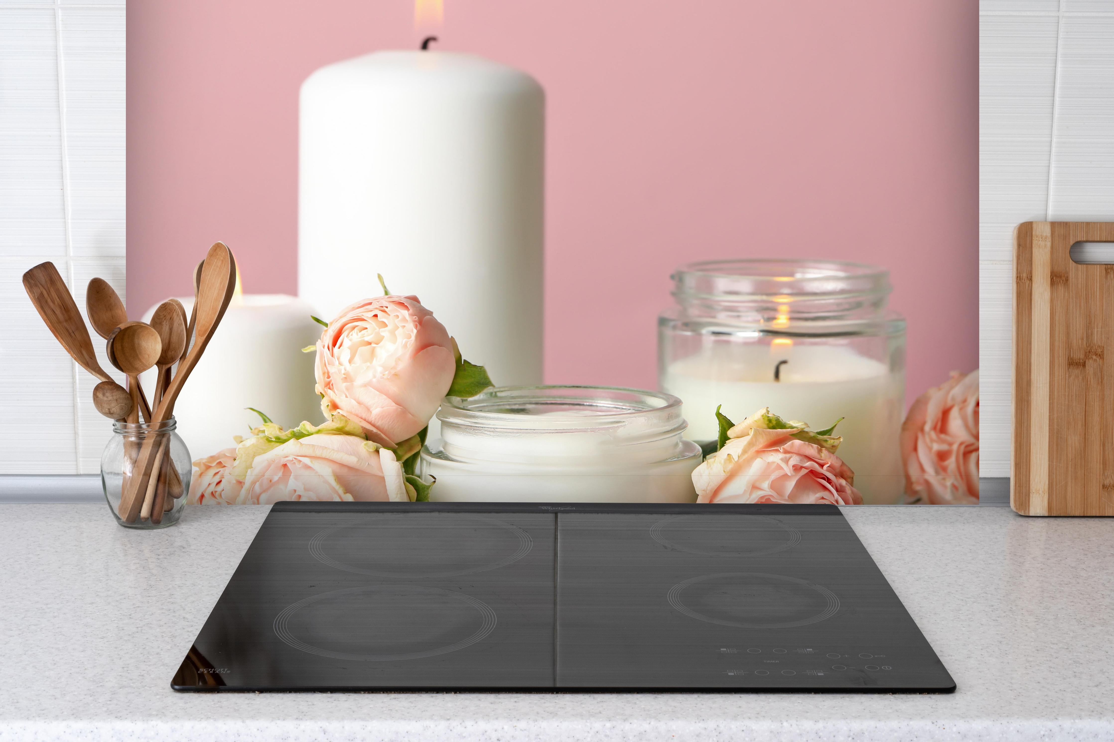 Spritzschutz - Duftkerzen und Rosen auf weißem Tisch hinter einem Cerankochfeld zwischen Holz-Kochutensilien