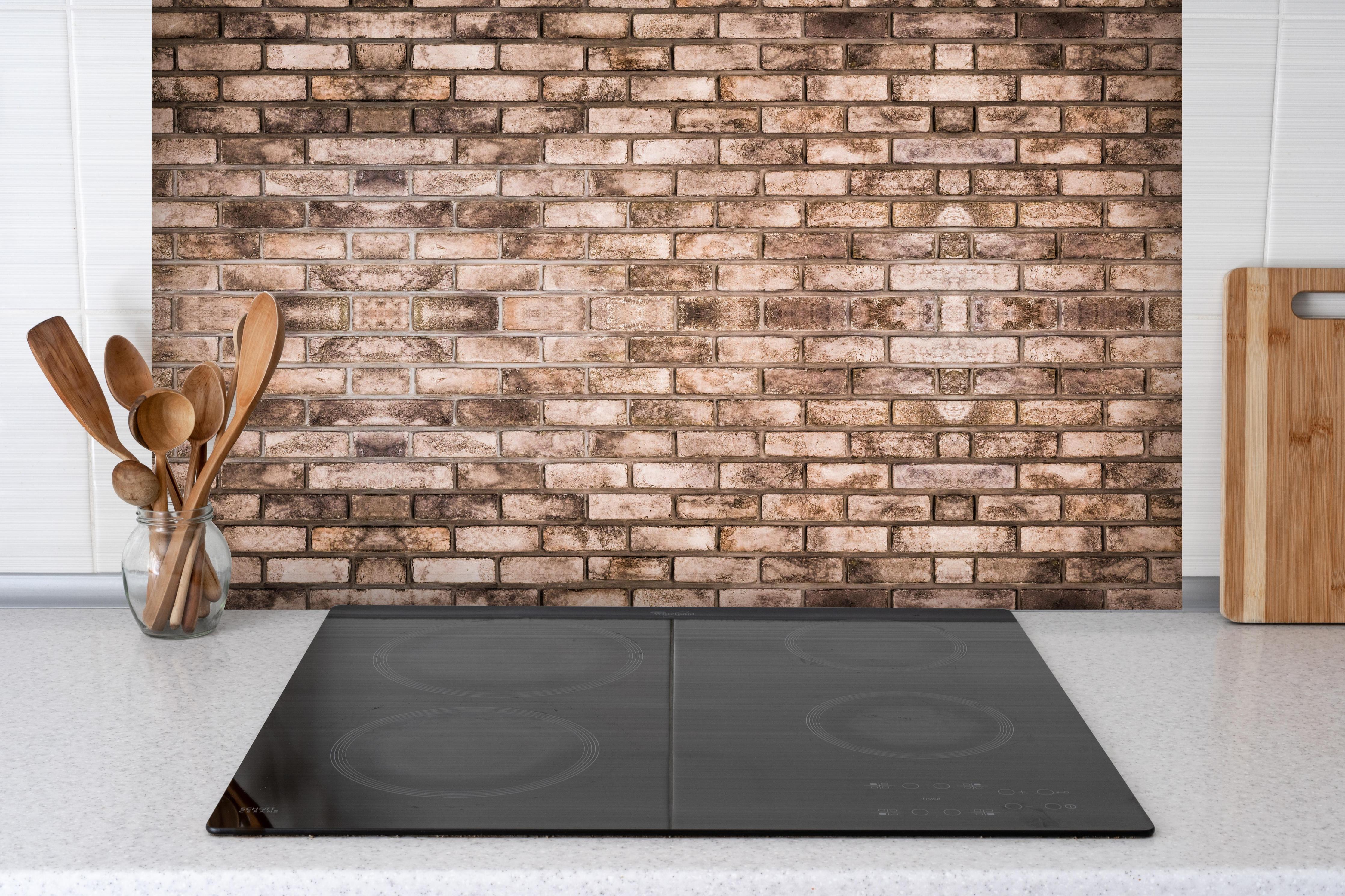 Spritzschutz - Dunkelbraune Steinmauer hinter einem Cerankochfeld zwischen Holz-Kochutensilien