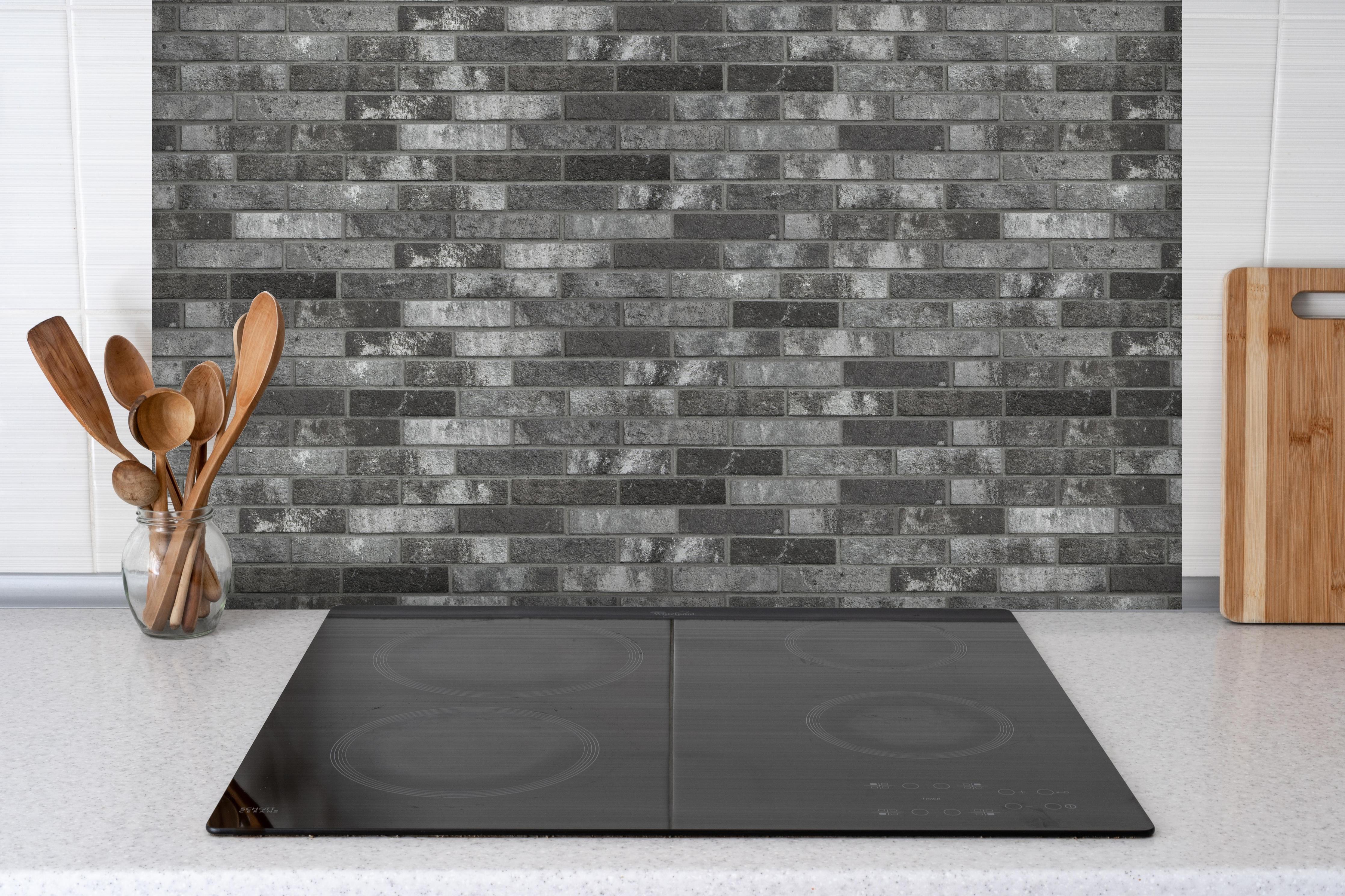 Spritzschutz - Dunkelgraue Backsteinmauer hinter einem Cerankochfeld zwischen Holz-Kochutensilien