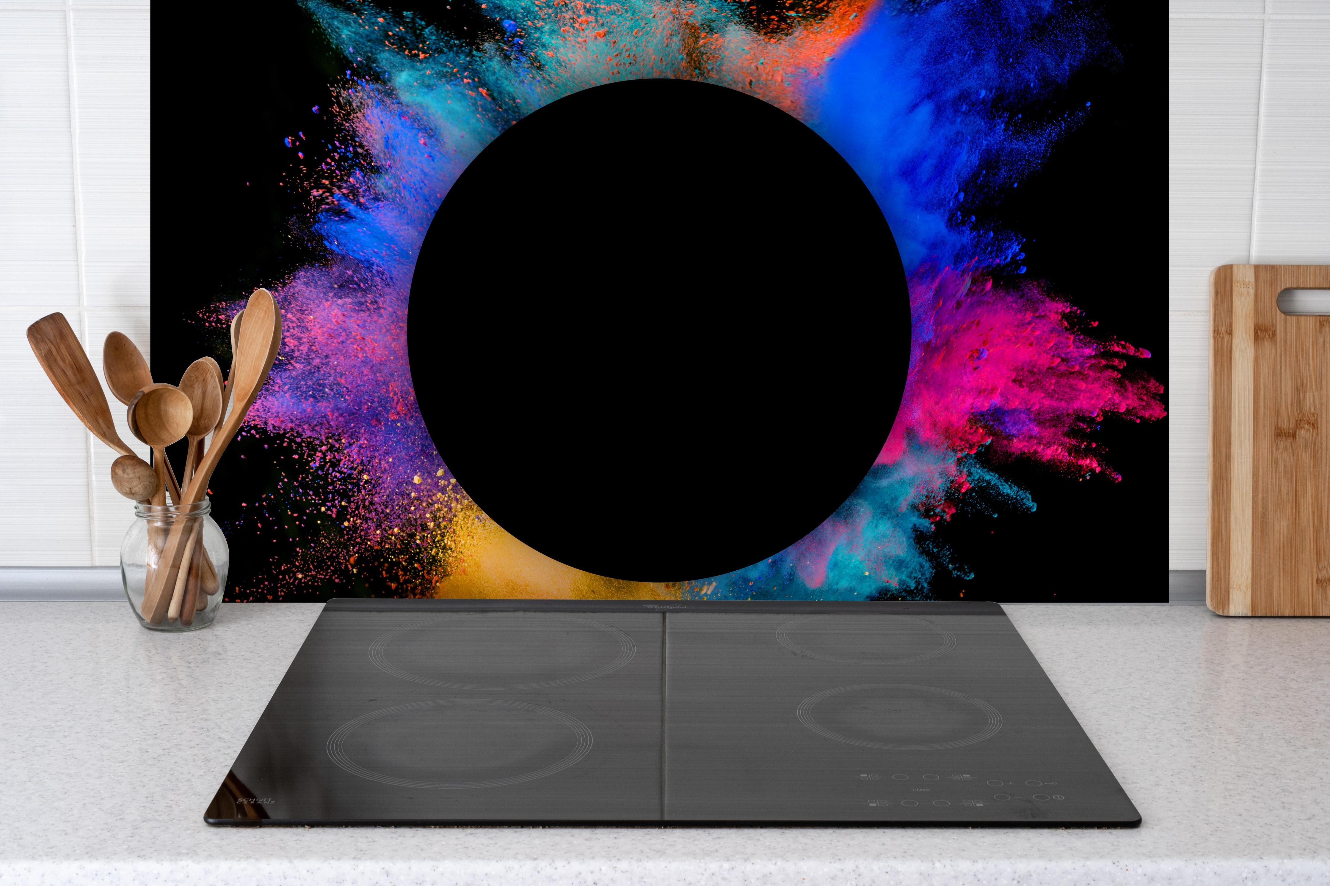 Spritzschutz - Explosion von farbigem Pulver mit schwarzem Kreis hinter einem Cerankochfeld zwischen Holz-Kochutensilien