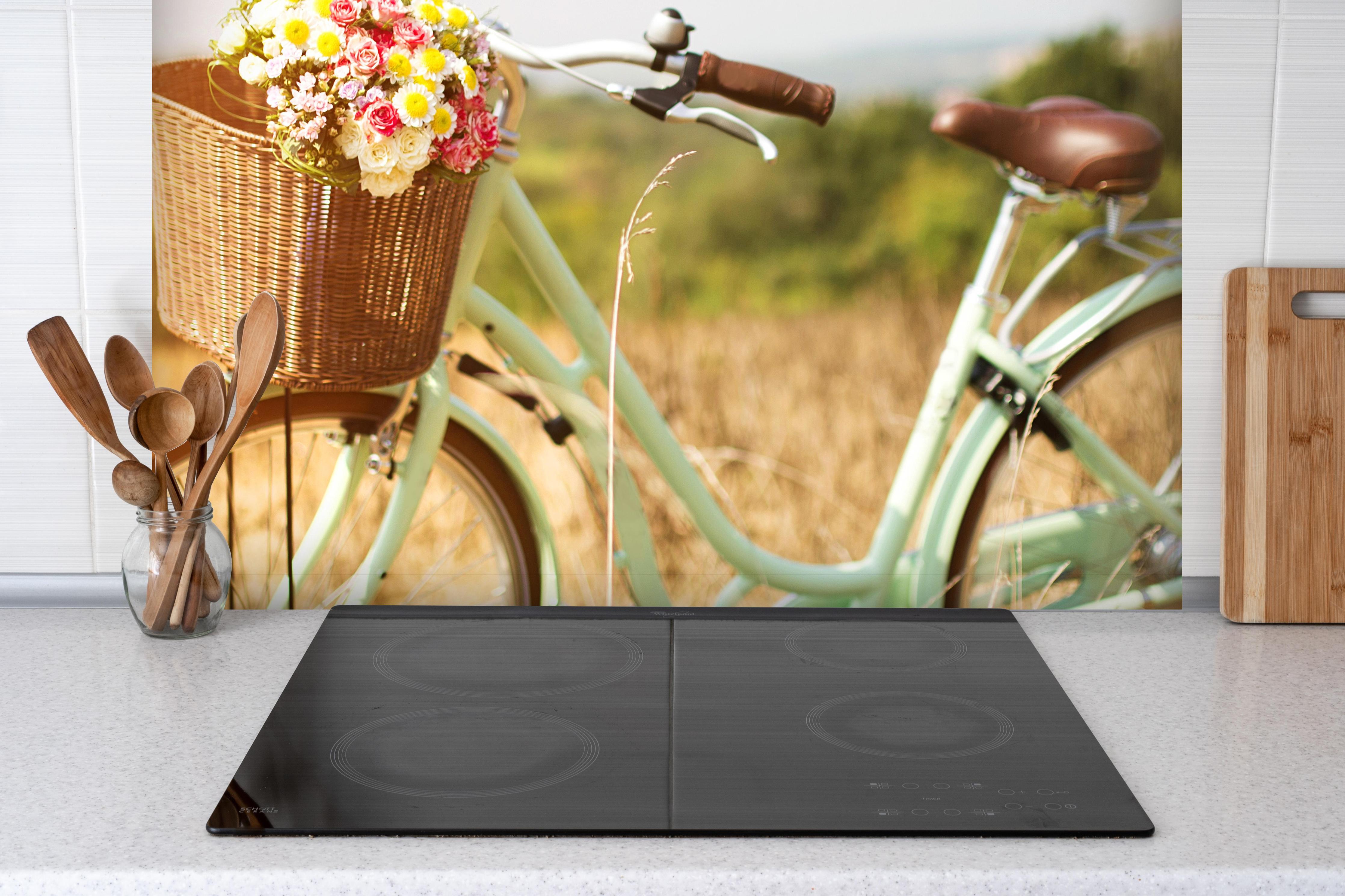 Spritzschutz - Fahrrad mit Blumenkorb auf Wiese hinter einem Cerankochfeld zwischen Holz-Kochutensilien