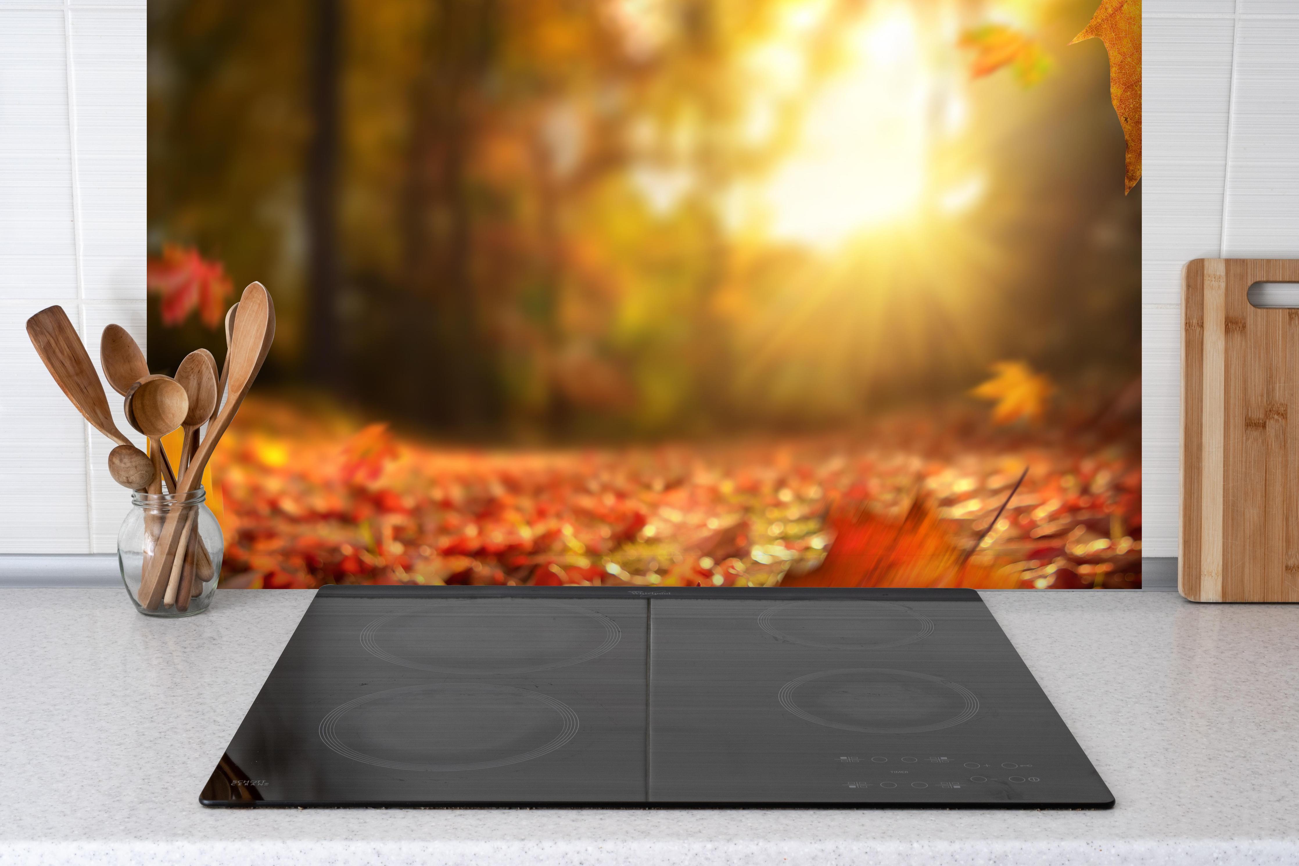 Spritzschutz - Fallende Blätter im Herbst hinter einem Cerankochfeld zwischen Holz-Kochutensilien