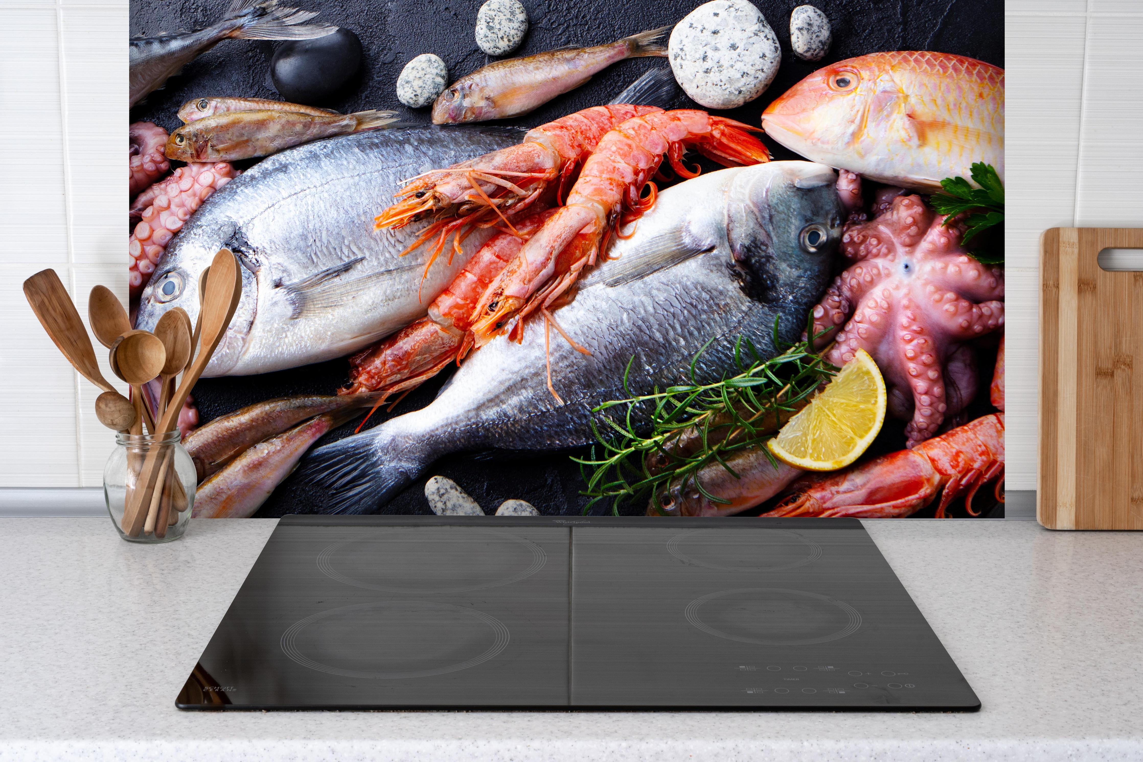 Spritzschutz - Fische & Meeresfrüchte auf Schieferstein hinter einem Cerankochfeld zwischen Holz-Kochutensilien
