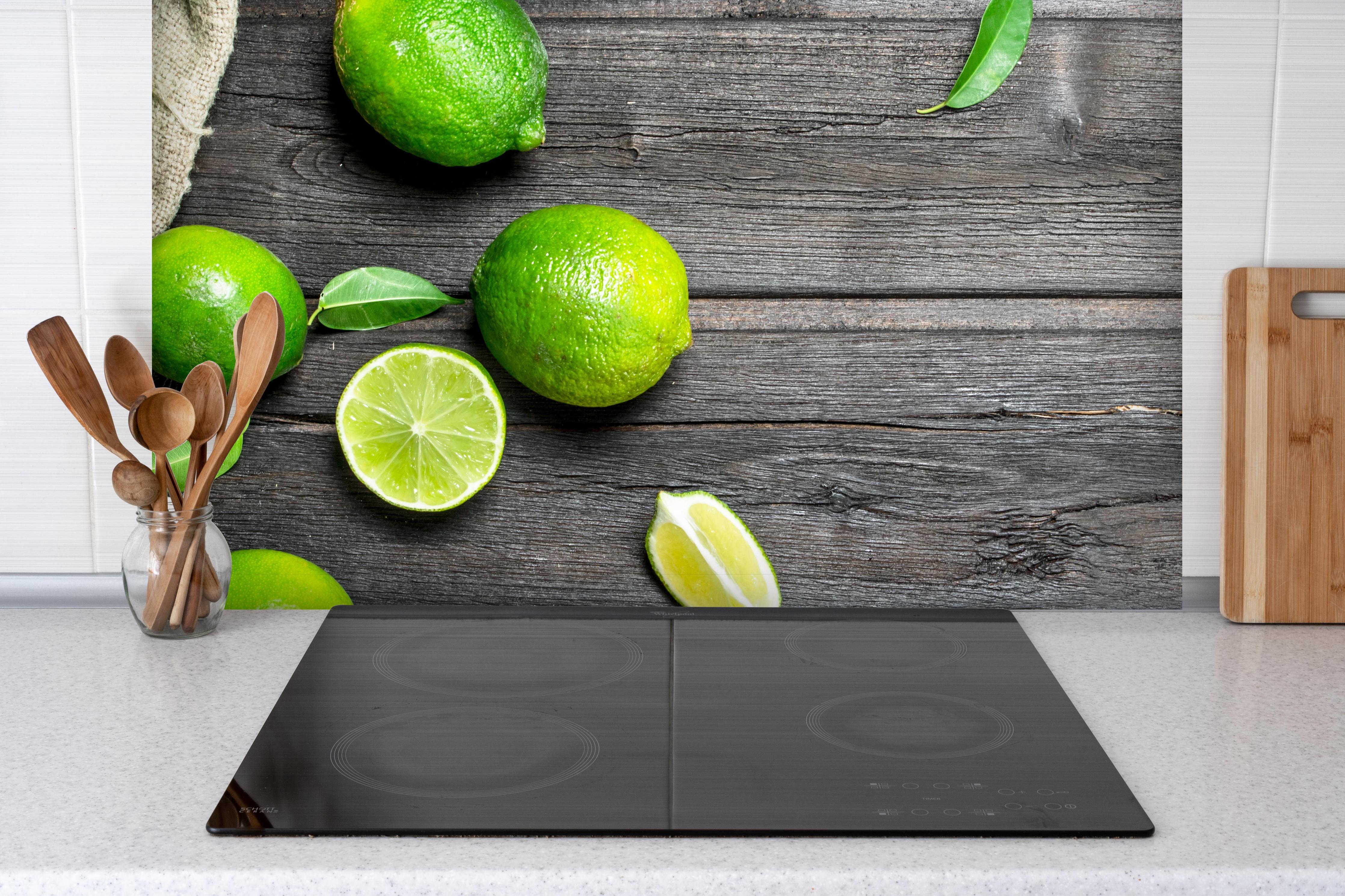 Spritzschutz - Frisch geerntete Limetten hinter einem Cerankochfeld zwischen Holz-Kochutensilien