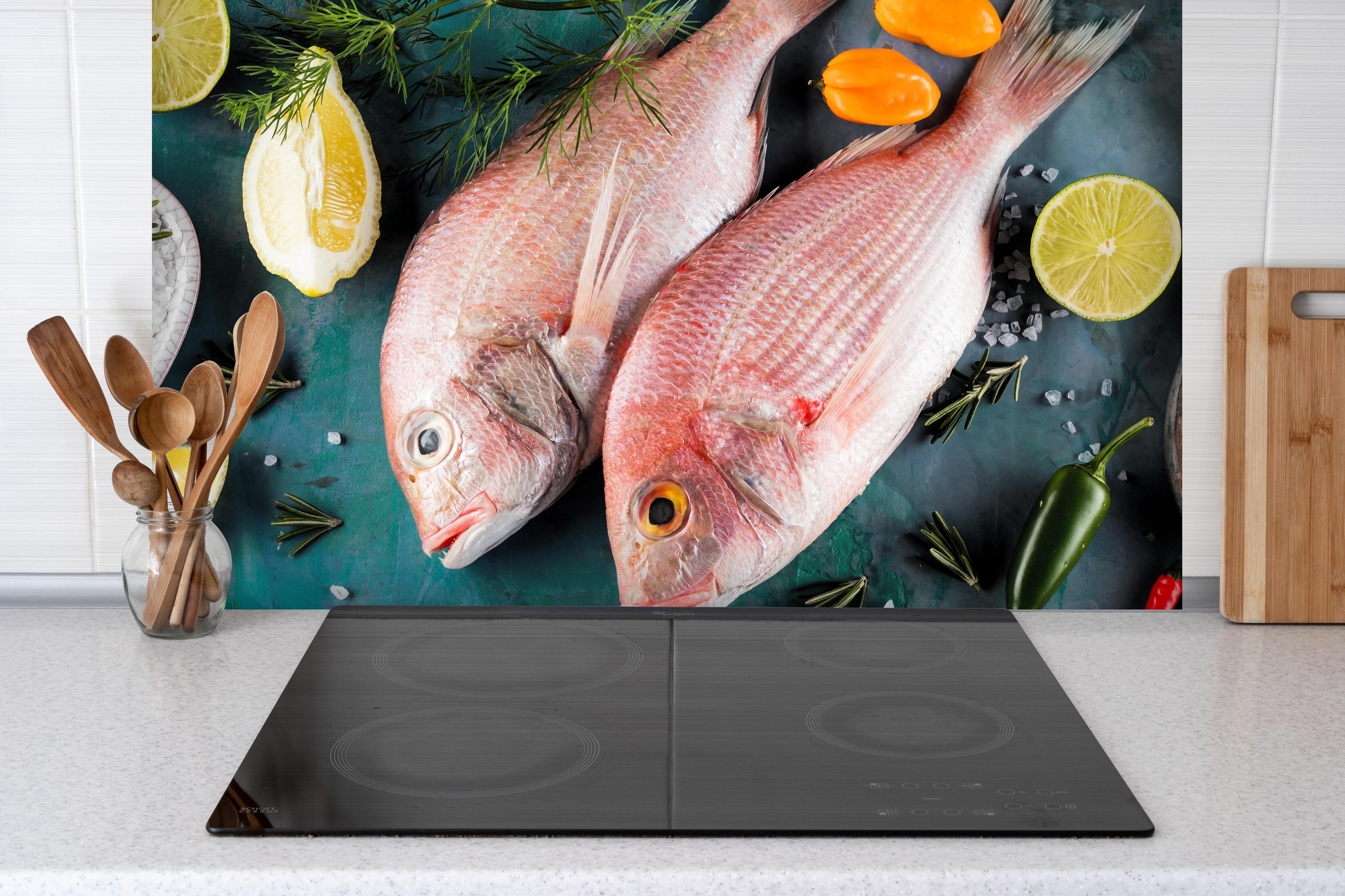 Spritzschutz - Frische Dorade hinter einem Cerankochfeld zwischen Holz-Kochutensilien