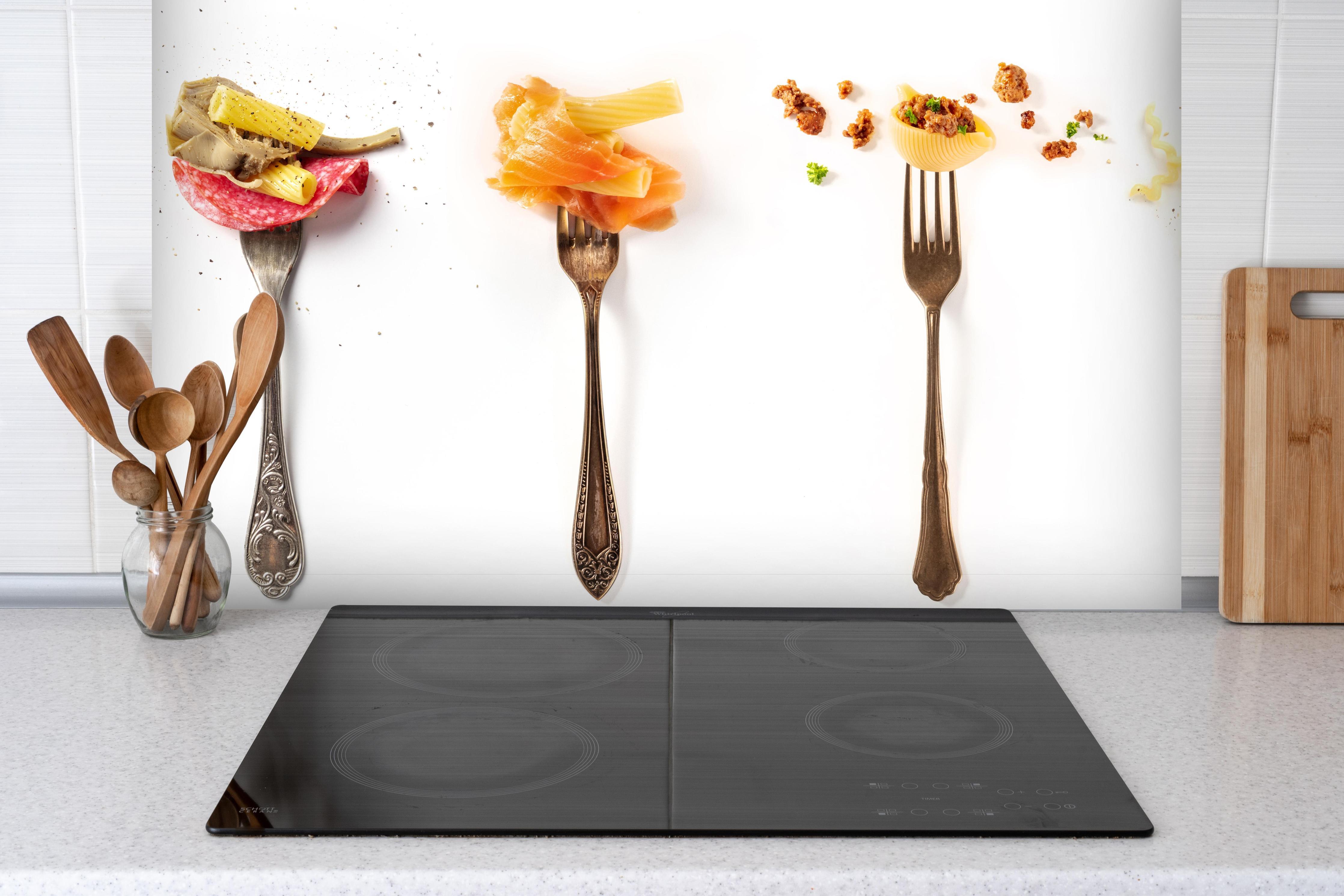 Spritzschutz - Gabeln mit Italienischer Pasta Essen hinter einem Cerankochfeld zwischen Holz-Kochutensilien