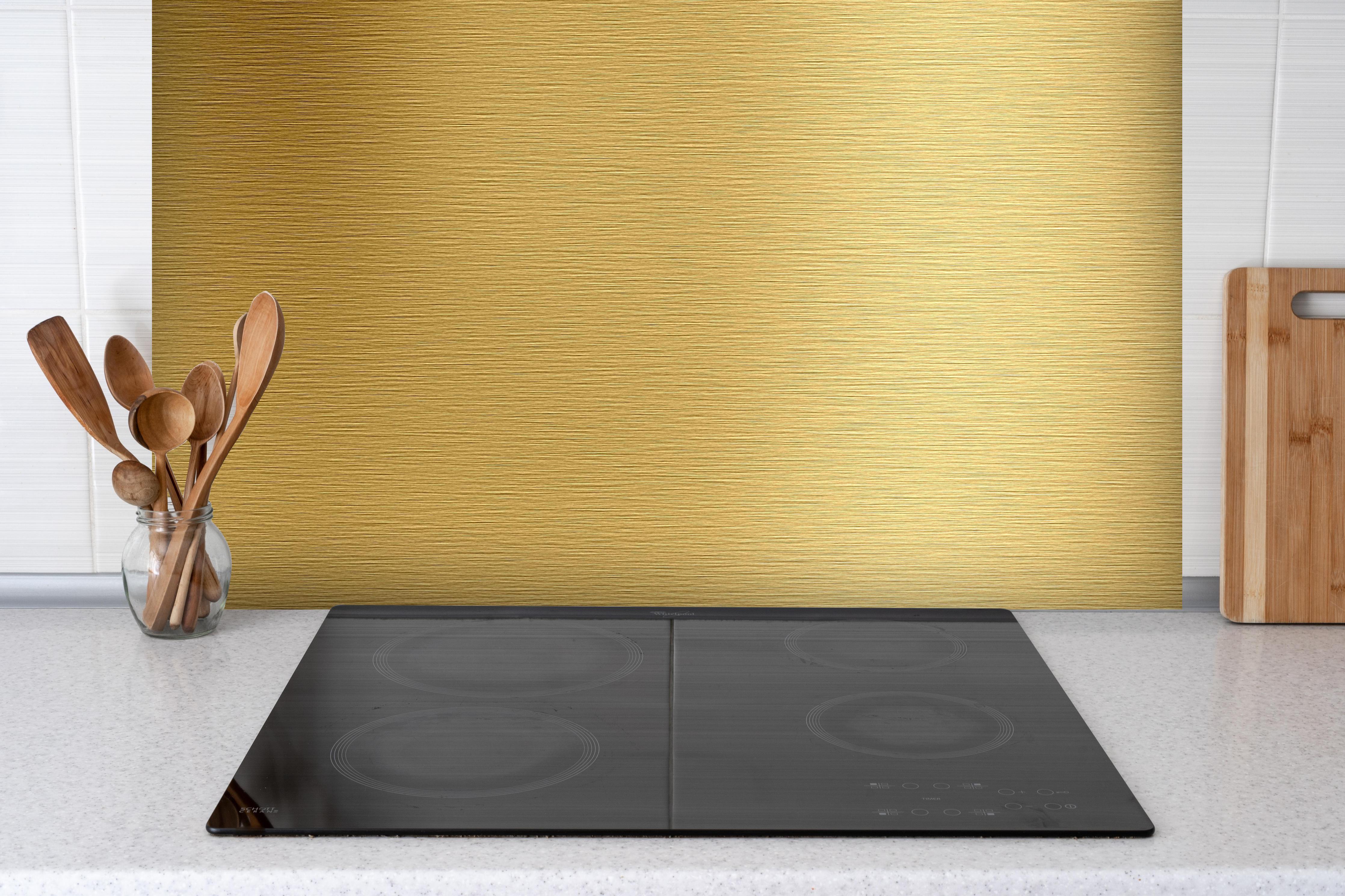 Spritzschutz - Gebürstetes Gold hinter einem Cerankochfeld zwischen Holz-Kochutensilien