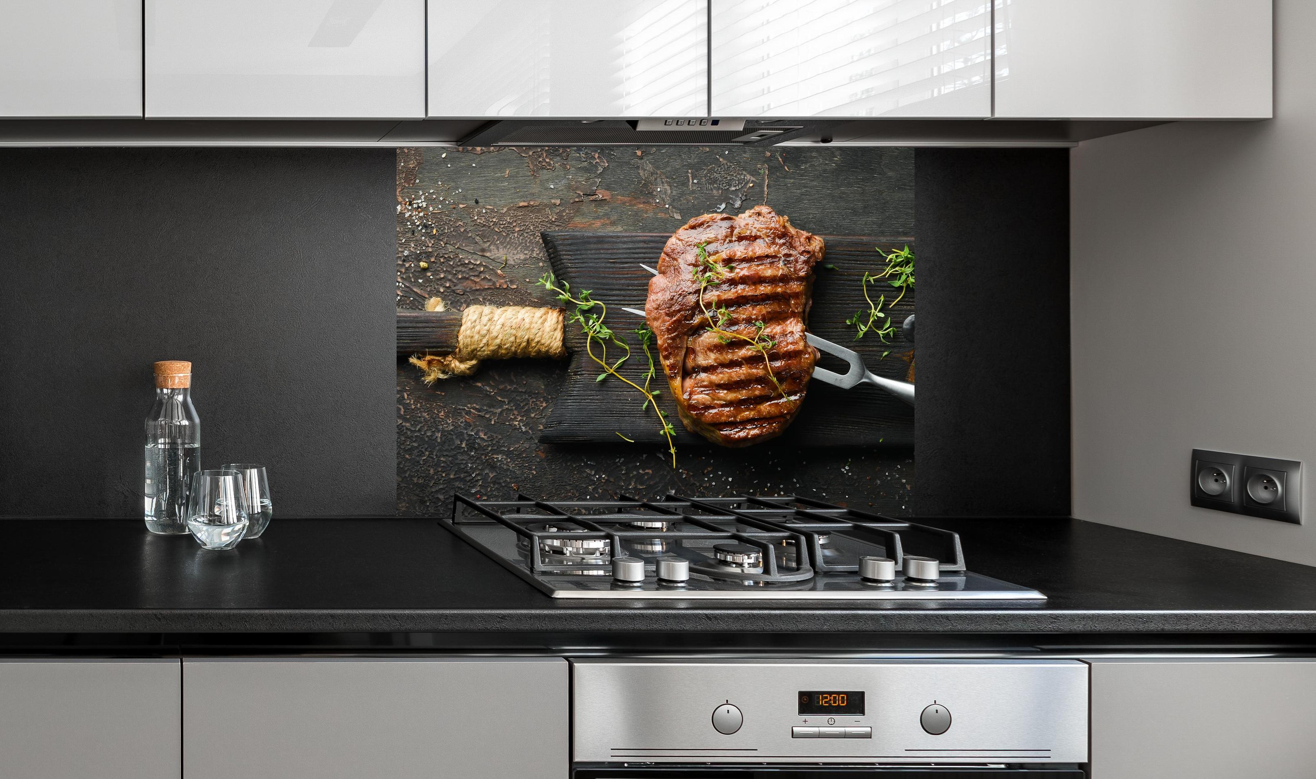 Spritzschutz - Gegrilltes Ribeye auf Holzplatte an edler Anthrazit-Wand hinter silbernem Gasherd