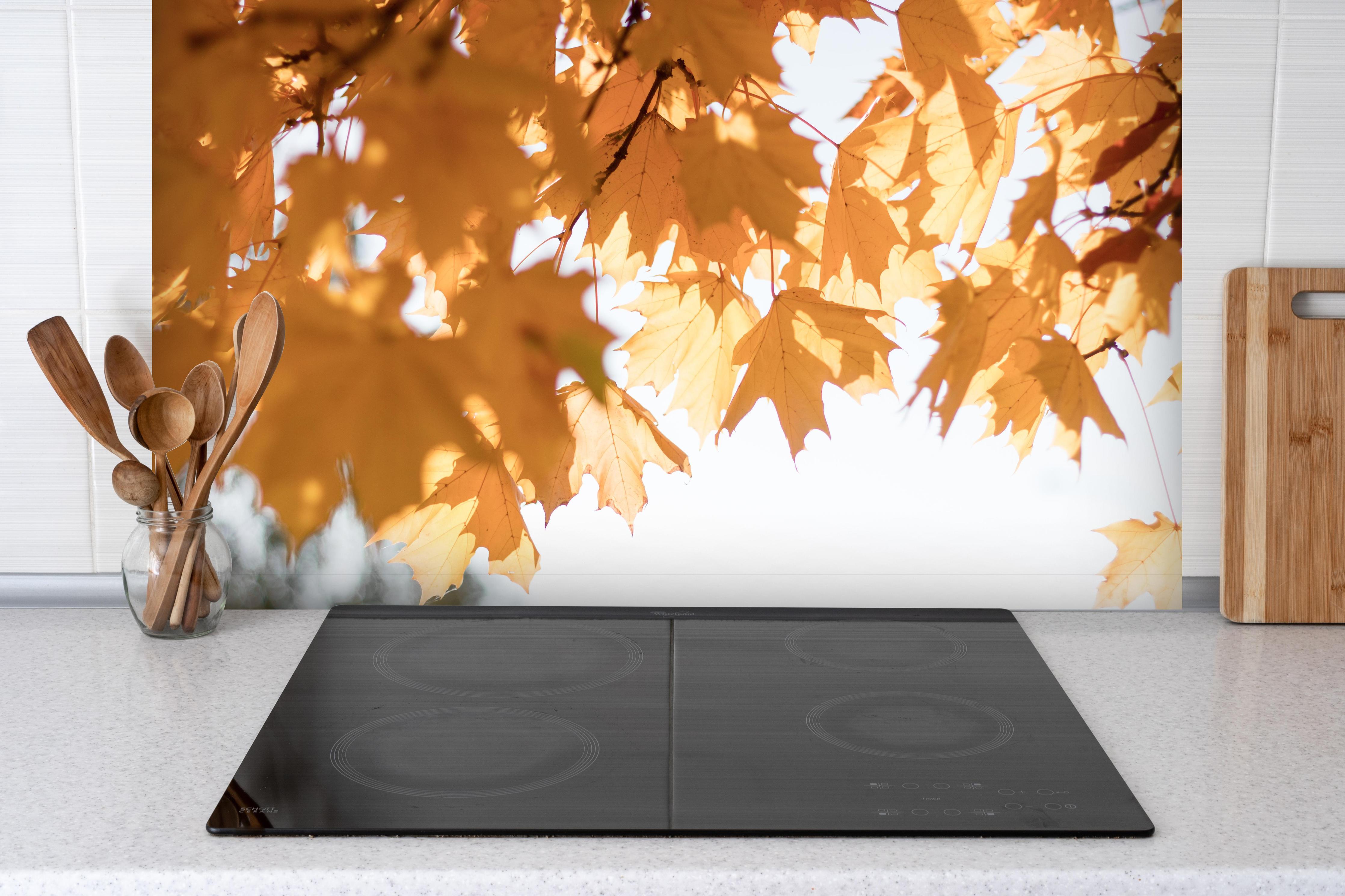 Spritzschutz - Gelben Ahornblättern im Herbst hinter einem Cerankochfeld zwischen Holz-Kochutensilien