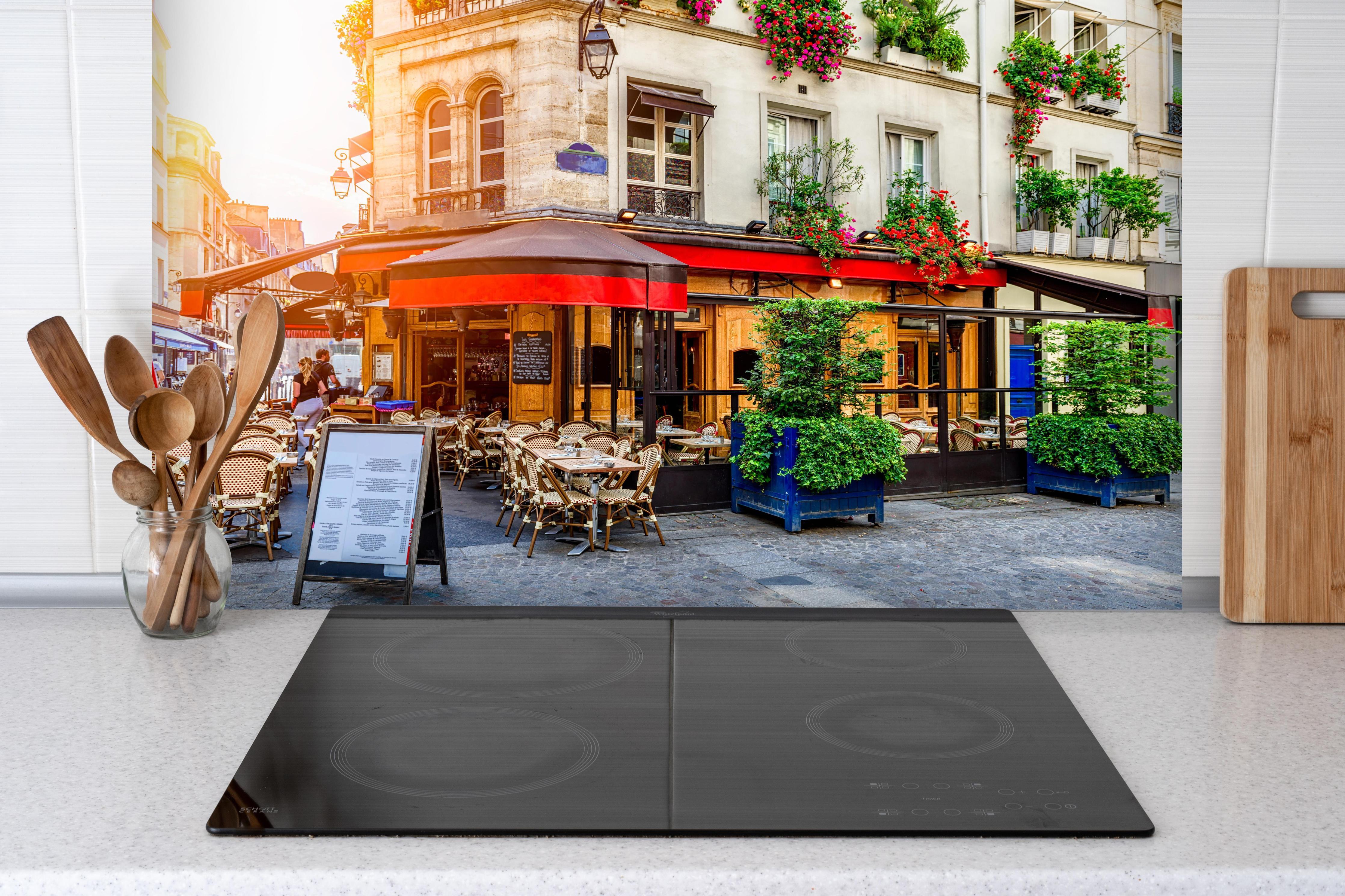 Spritzschutz - Gemütliche Straße mit Tischen eines Cafés in Paris hinter einem Cerankochfeld zwischen Holz-Kochutensilien