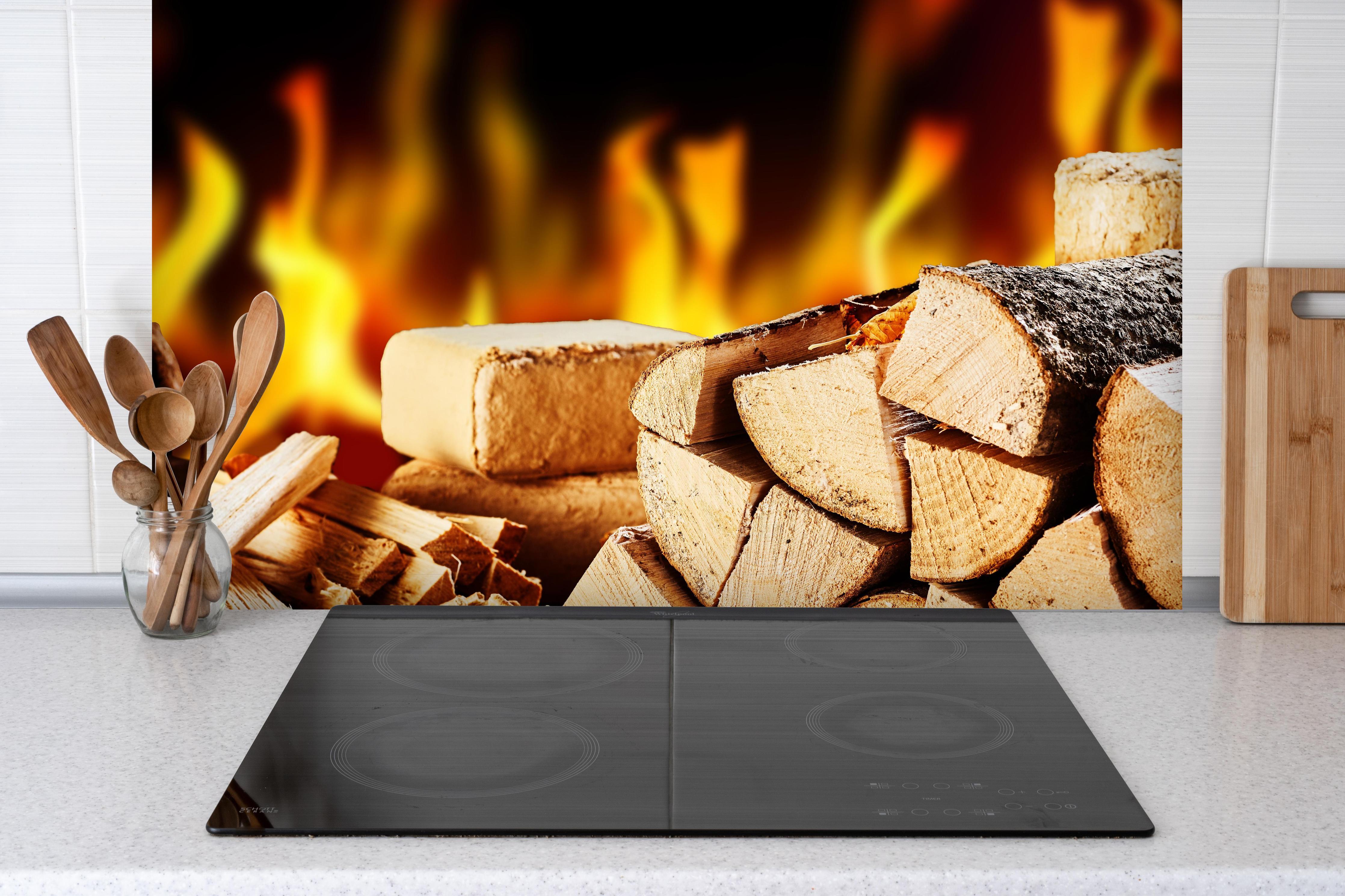 Spritzschutz - Gestapelte Holzscheite vor brennendem Feuer hinter einem Cerankochfeld zwischen Holz-Kochutensilien