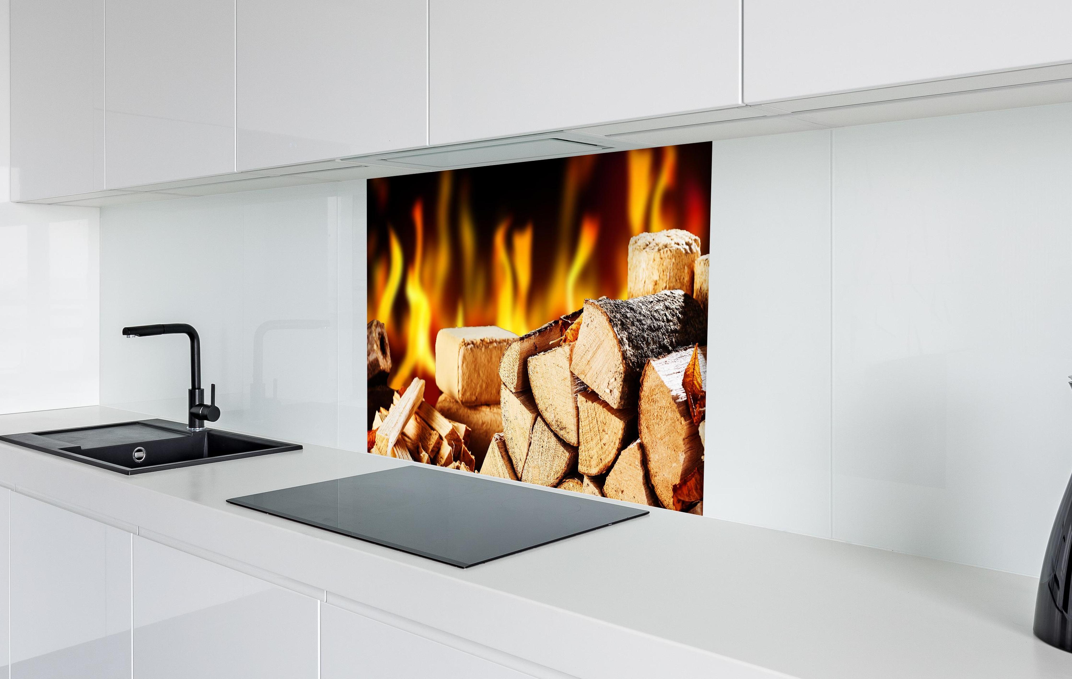 Spritzschutz - Gestapelte Holzscheite vor brennendem Feuer in weißer Hochglanz-Küche hinter einem Cerankochfeld