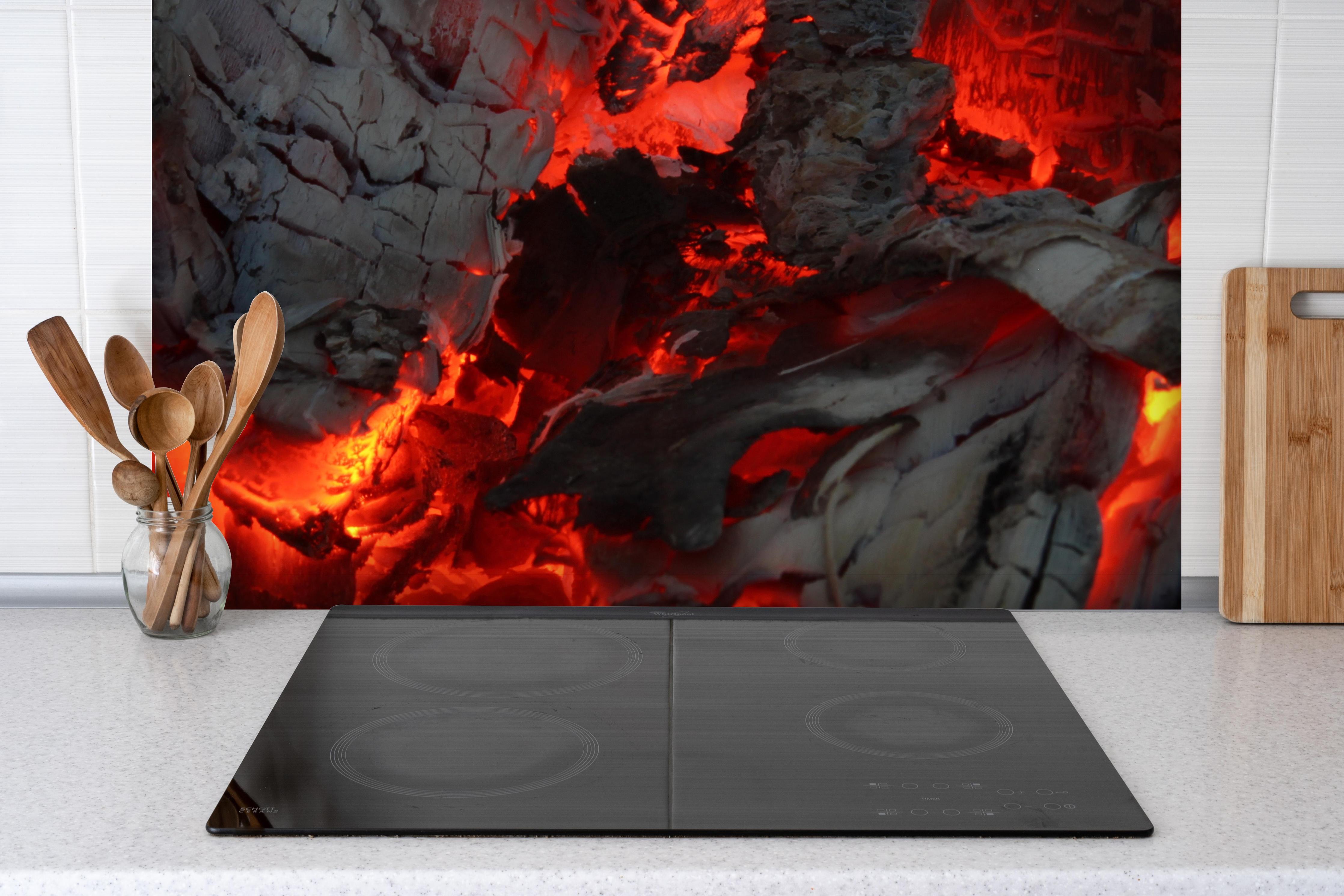 Spritzschutz - Glühendes Feuer - Nahaufnahme hinter einem Cerankochfeld zwischen Holz-Kochutensilien