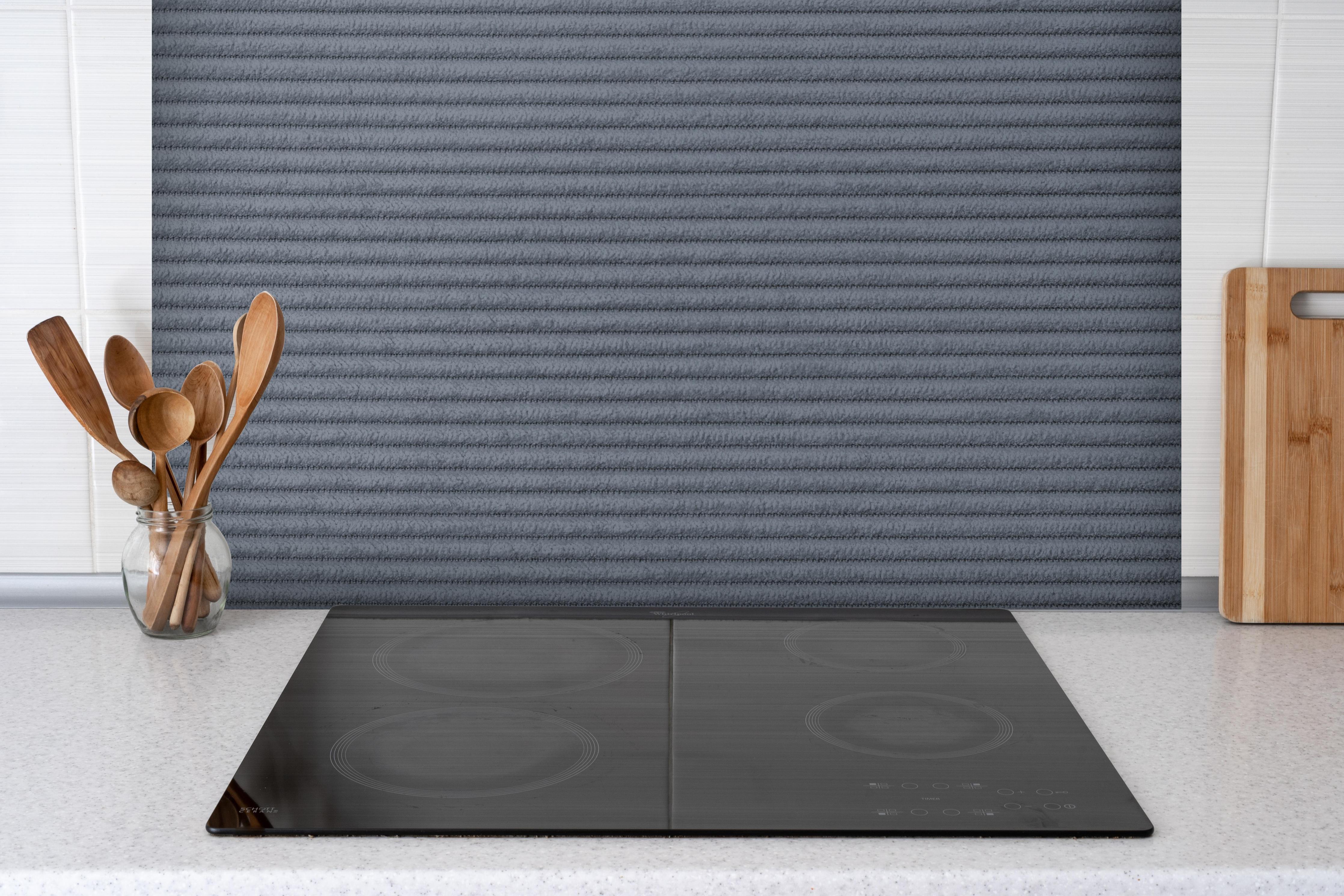 Spritzschutz - Gräulicher genähter Stoff hinter einem Cerankochfeld zwischen Holz-Kochutensilien