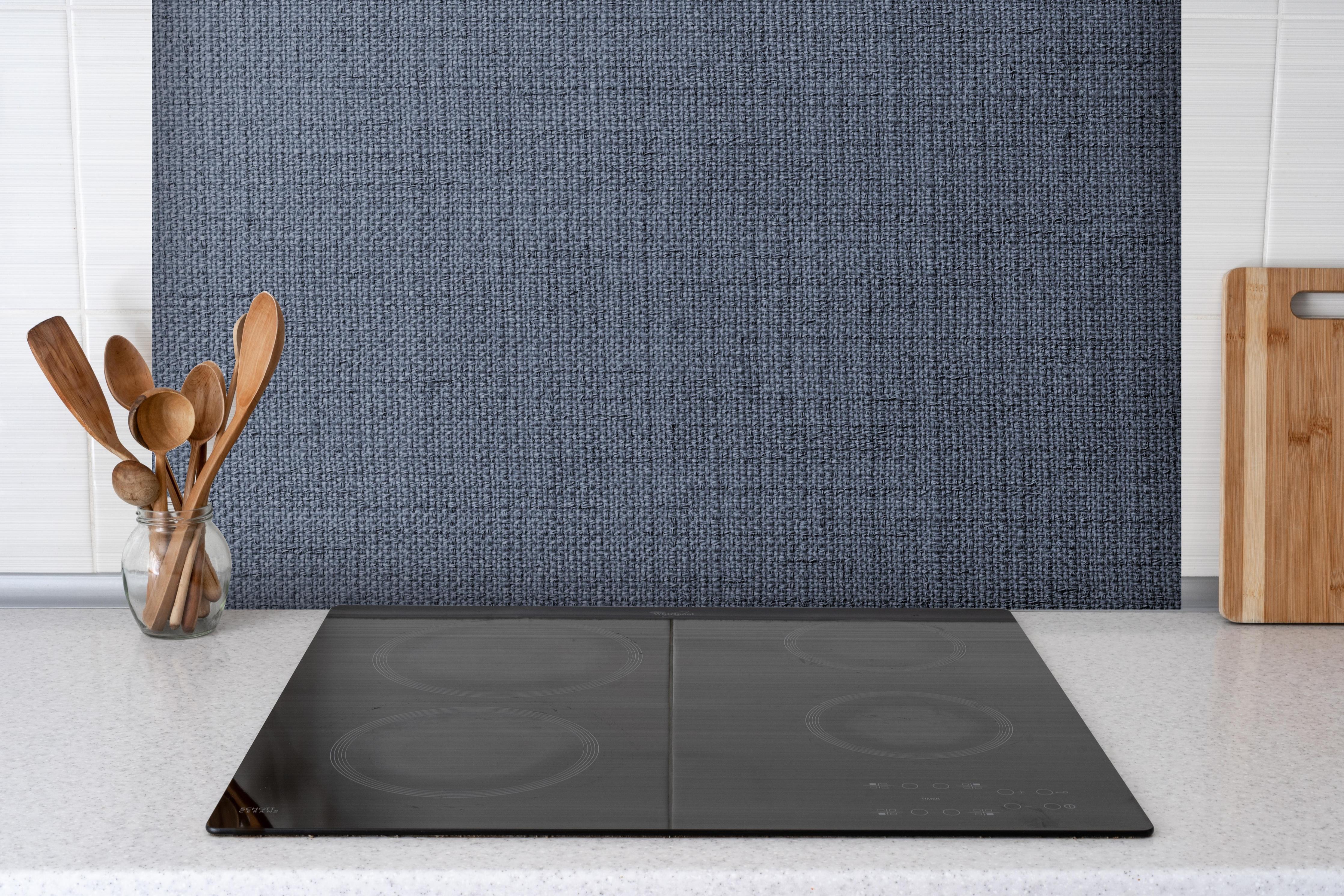 Spritzschutz - Gräulicher gewebter Stoff hinter einem Cerankochfeld zwischen Holz-Kochutensilien