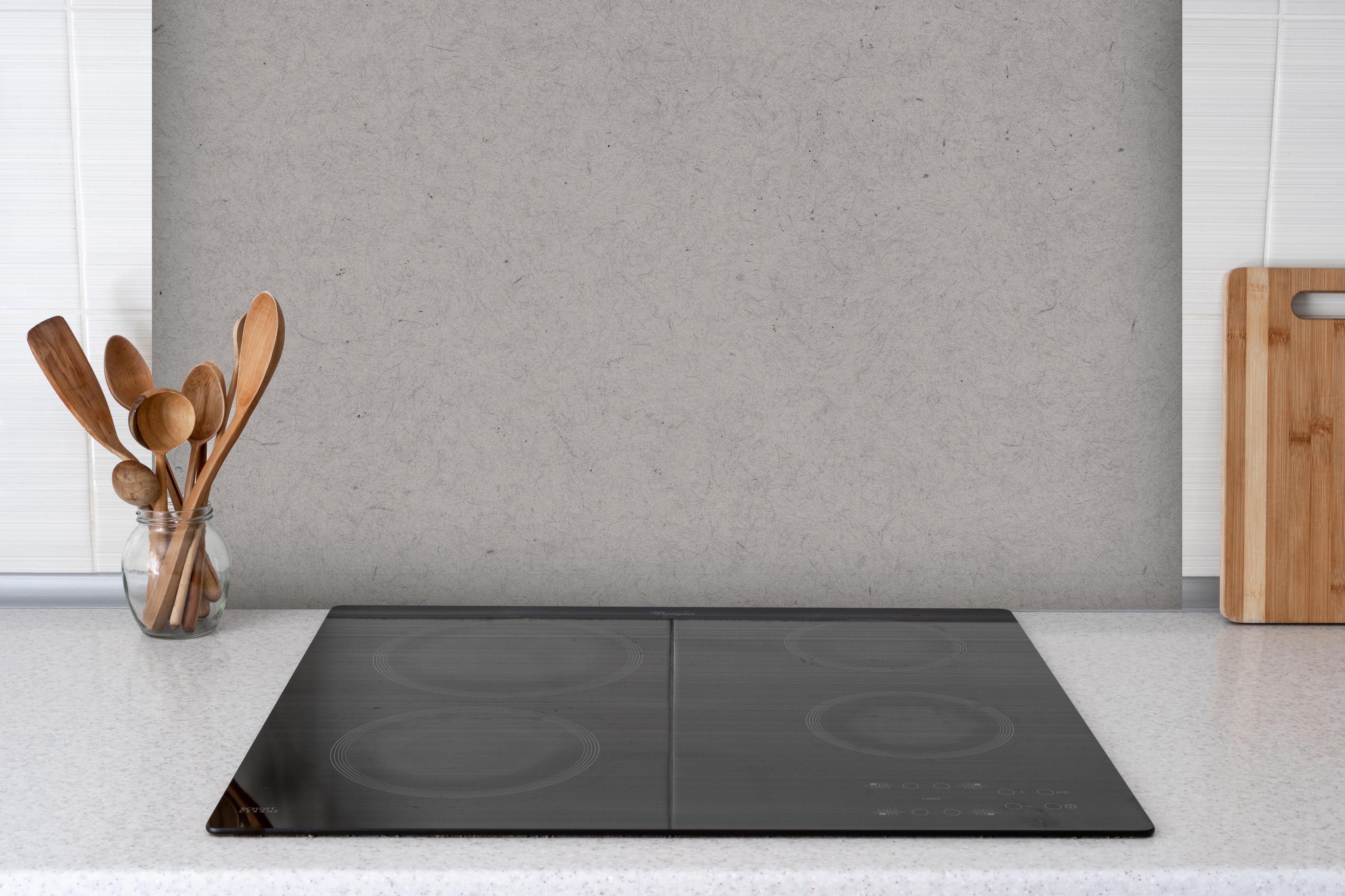 Spritzschutz - Gräuliches Papier hinter einem Cerankochfeld zwischen Holz-Kochutensilien