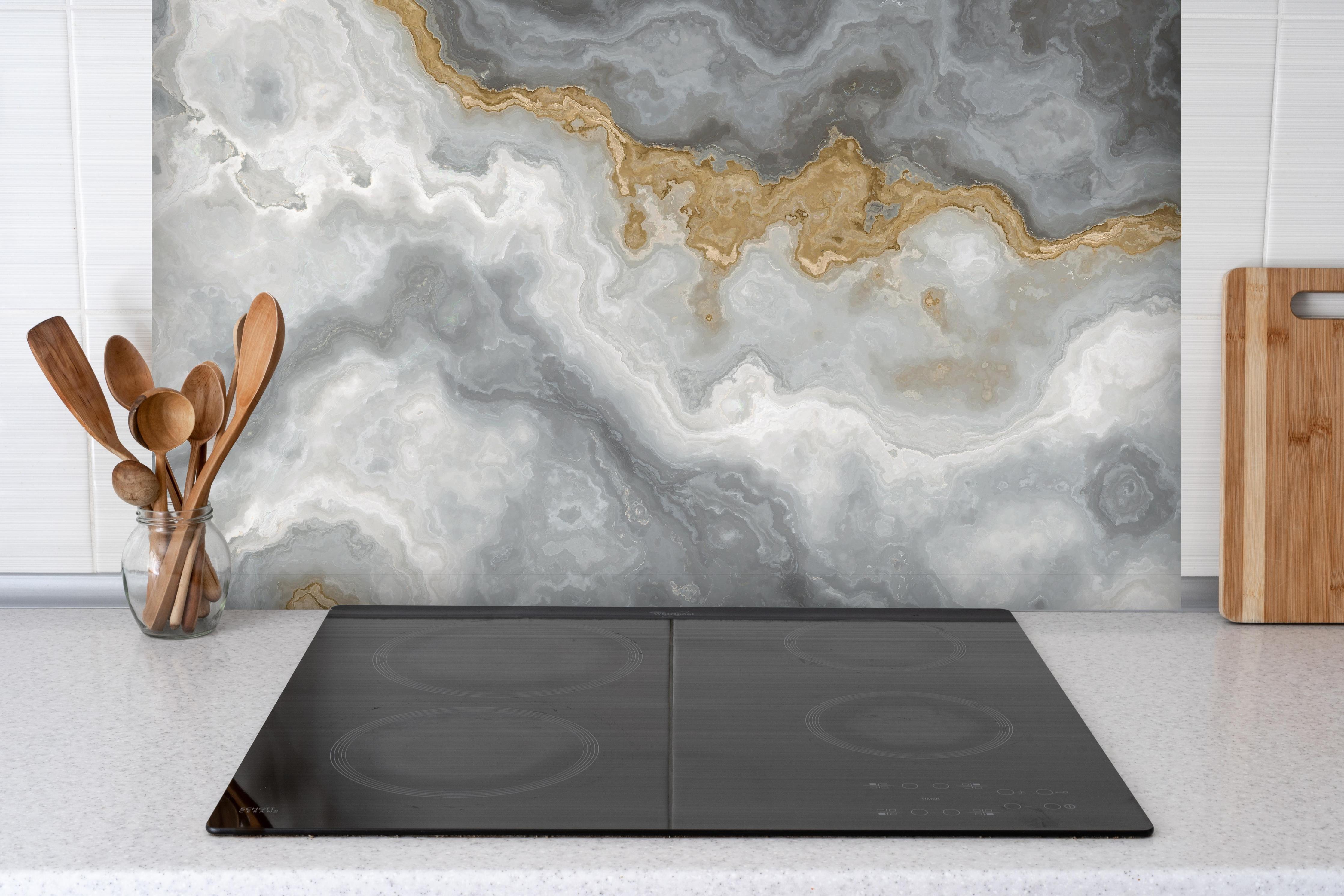 Spritzschutz - Grau-weißes Marmormuster hinter einem Cerankochfeld zwischen Holz-Kochutensilien